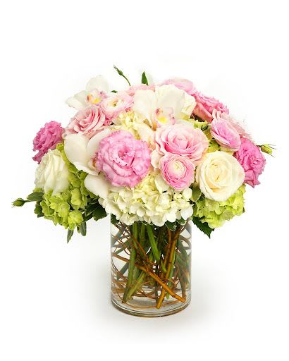 Round arrangement of pink and white roses, hydrangeas, and other blooms in a clear glass cylinder vase