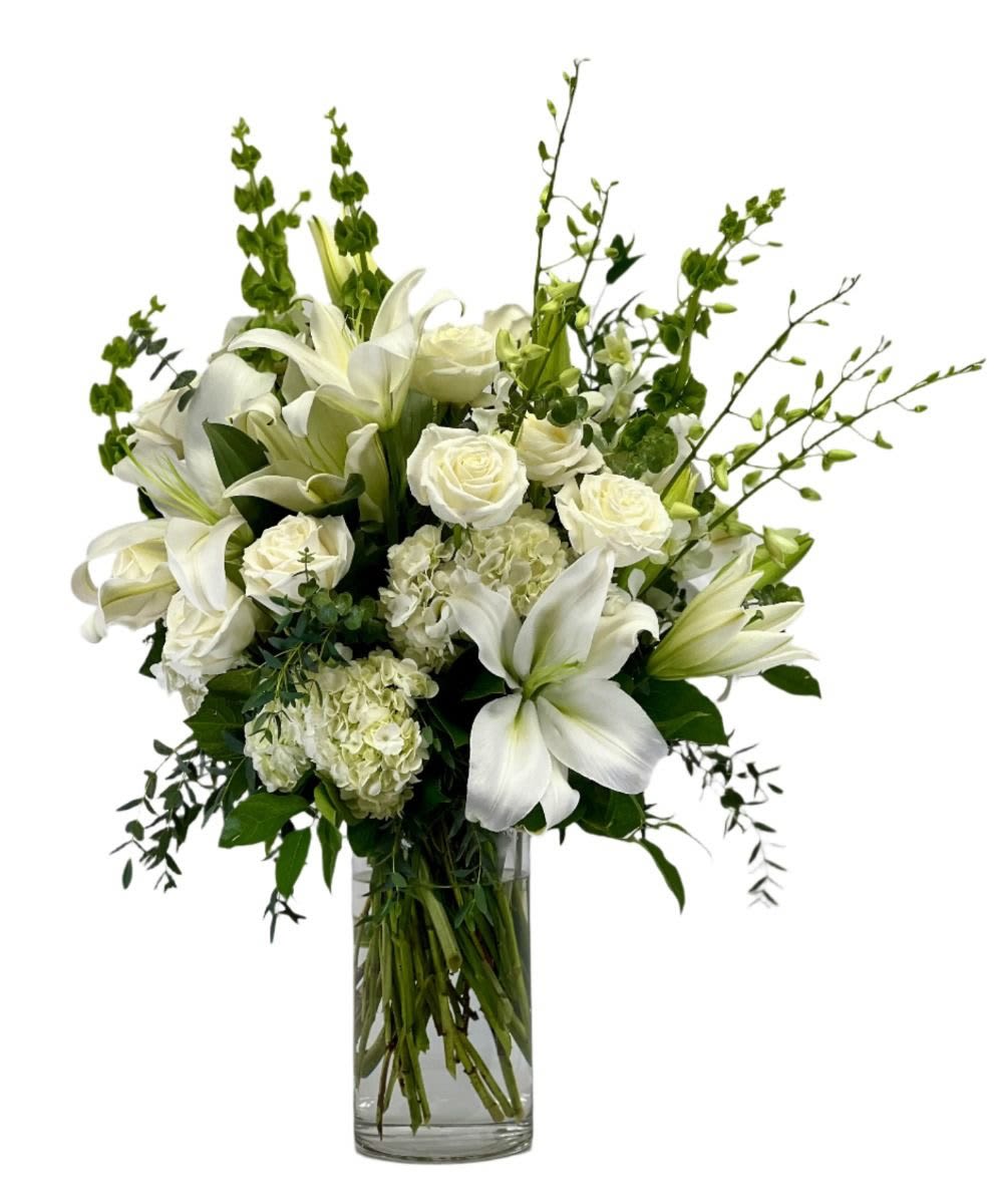 Tall arrangement of white lilies, roses, hydrangeas, and bells of Ireland in a clear glass vase