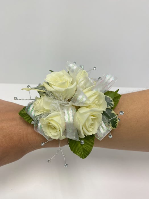 Wrist corsage of ivory roses with iridescent ribbon and crystal bead accents on an arm.