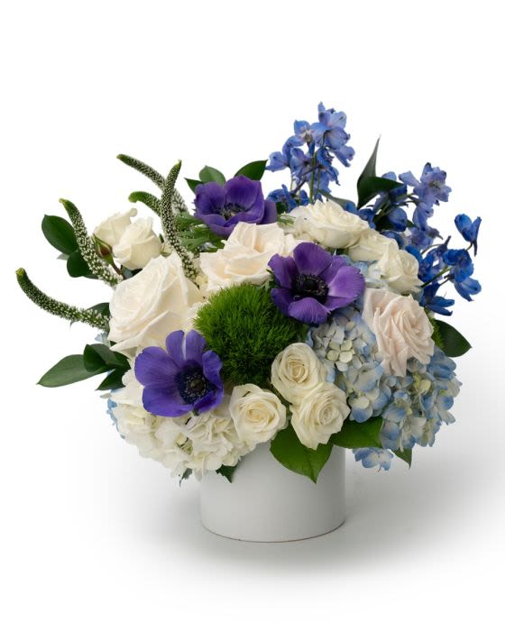 Low white vase of white roses, blue hydrangeas, and purple anemones