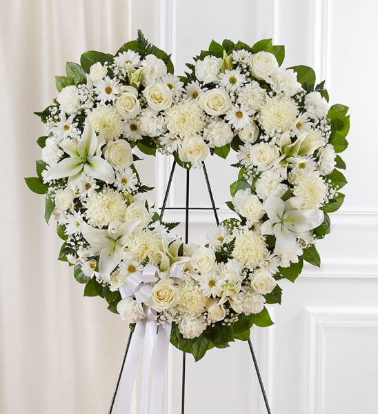 Heart-shaped white floral wreath with lilies and roses on a stand
