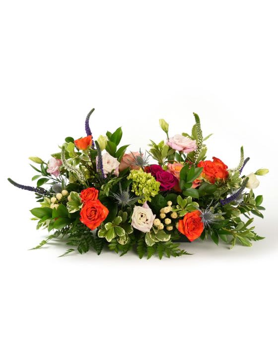 Low centerpiece of bright orange and pink roses with mixed blooms and berries in a horizontal arrangement