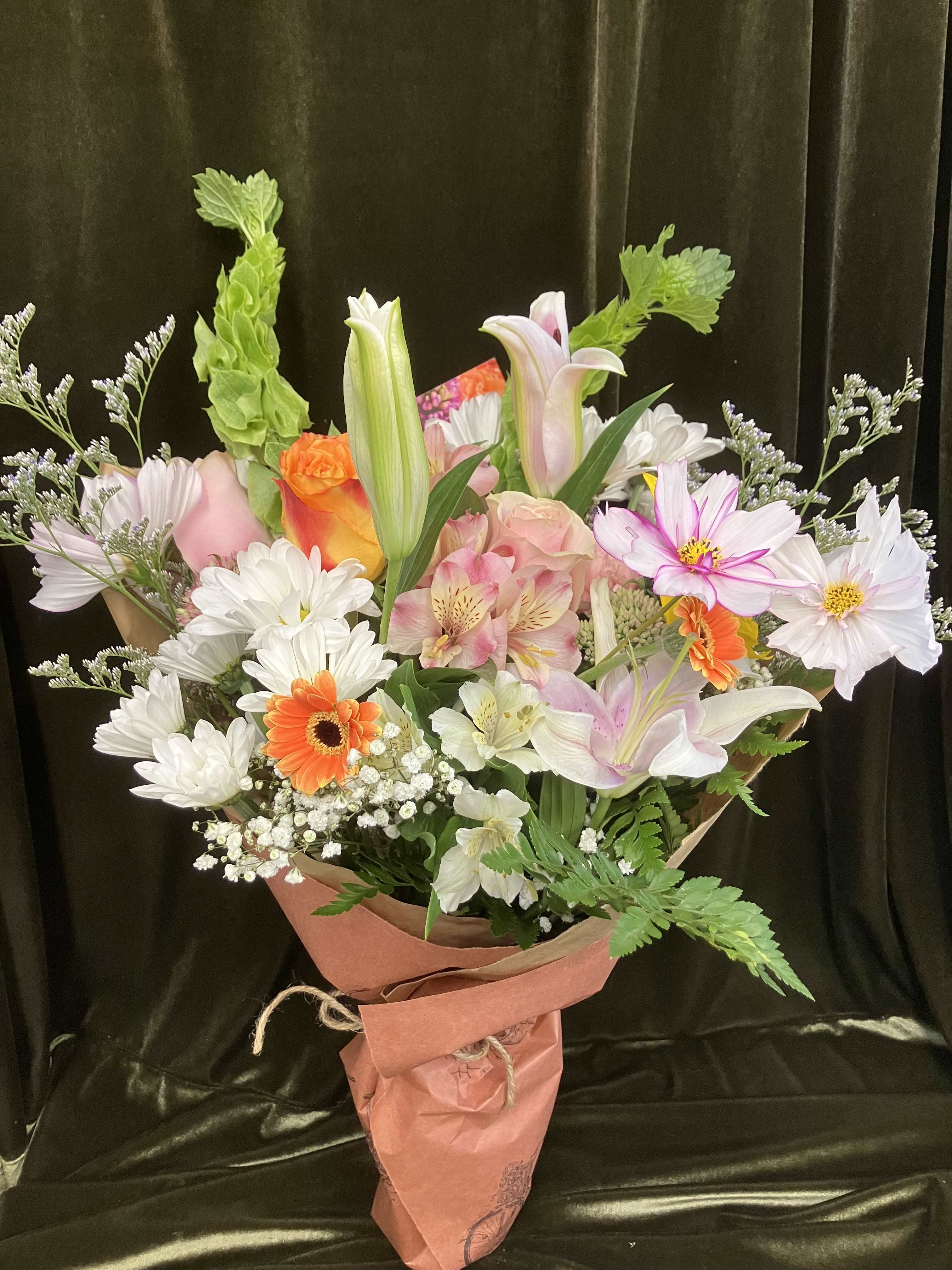 Mixed bouquet of lilies, roses, daisies, and orange gerbera daisies wrapped in pink paper