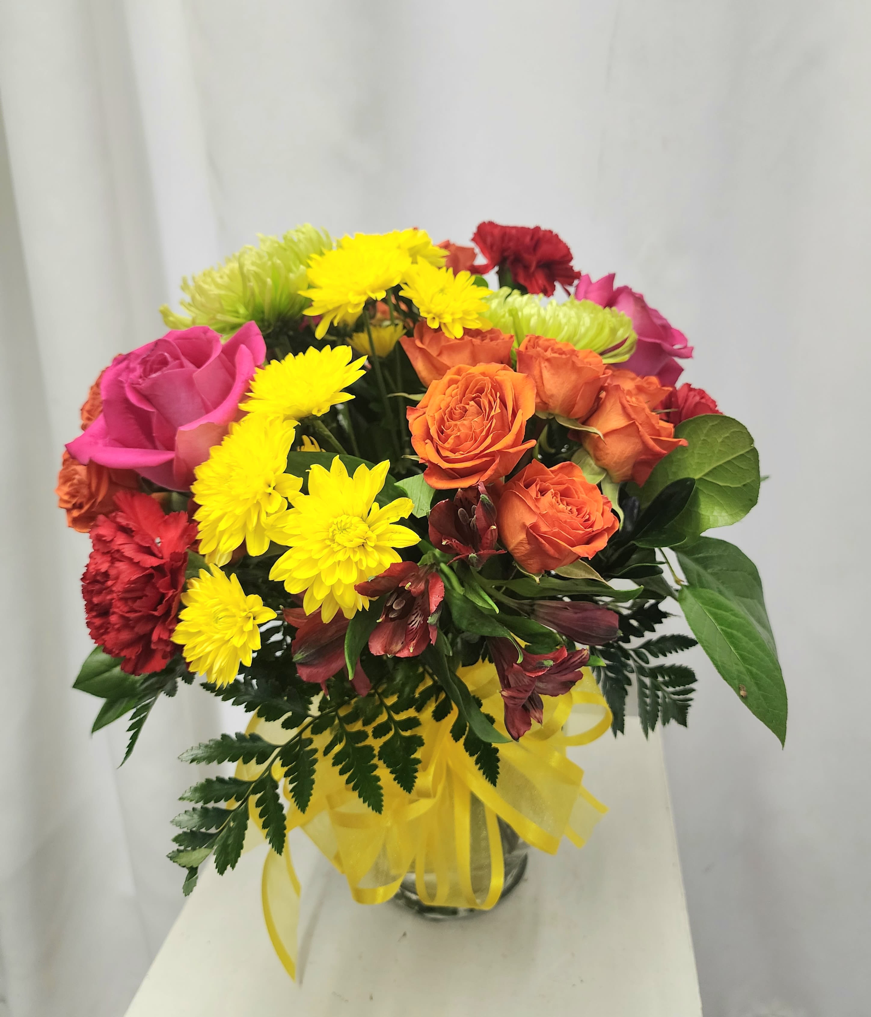 Mixed bouquet of roses and yellow chrysanthemums in a glass vase with a yellow ribbon