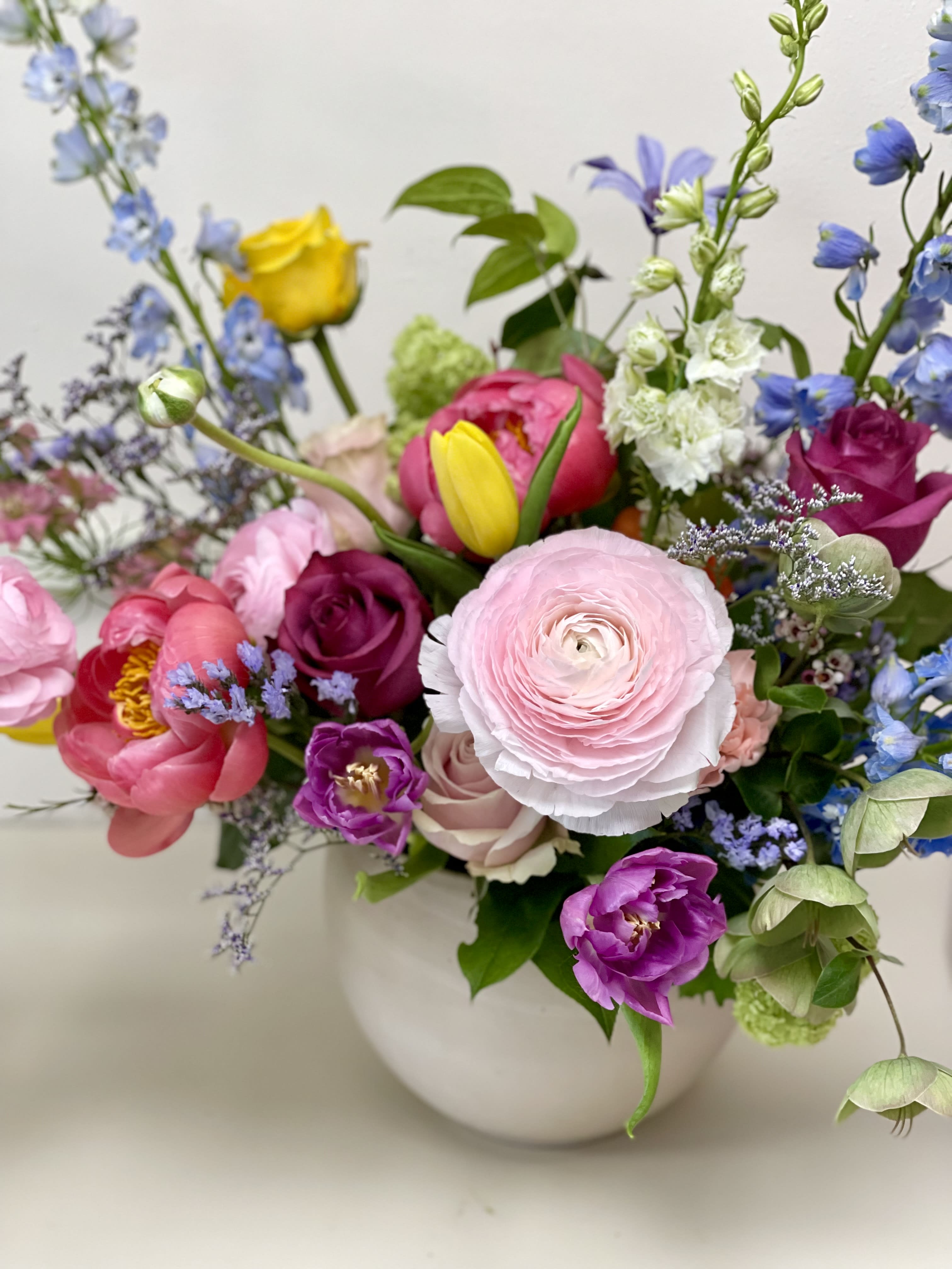 Mixed bouquet of pink, purple, yellow, and blue flowers in a white vase