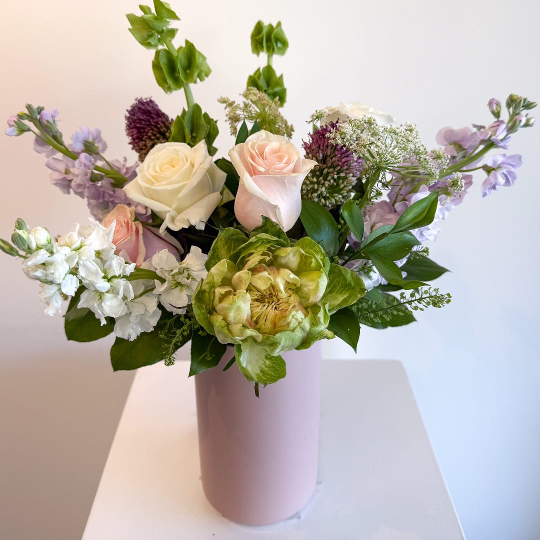Mixed bouquet of roses, green blooms, and lavender flowers in a pink vase