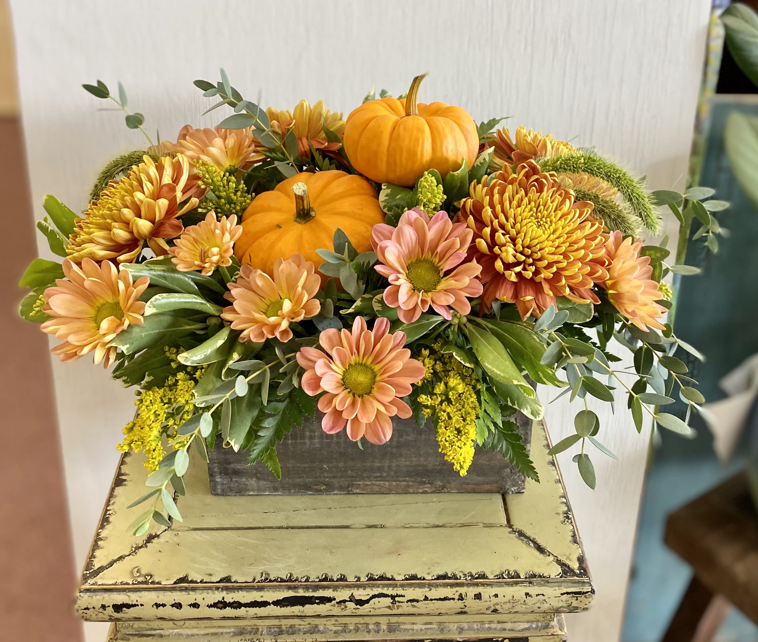 Autumn floral arrangement with orange pumpkins and peach chrysanthemums in a wooden box
