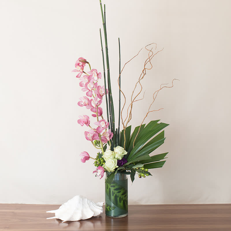 Tall modern arrangement with pink orchids and white roses in a clear cylinder vase