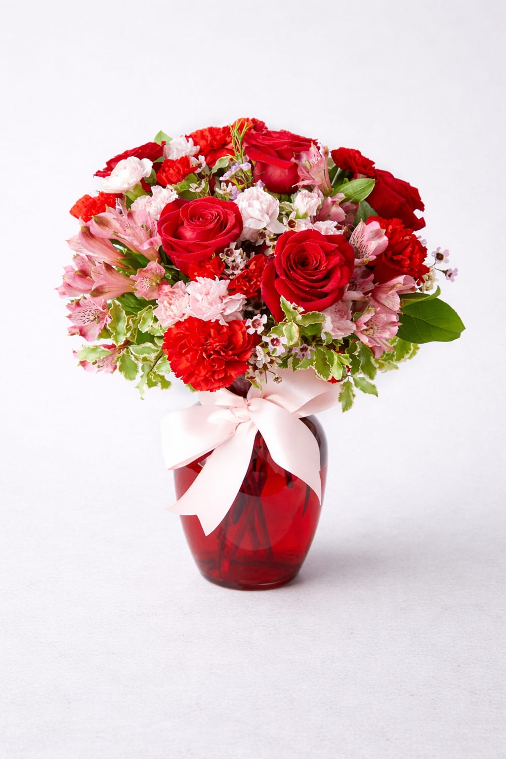 Red roses and pink carnations in a red glass vase with a pink ribbon