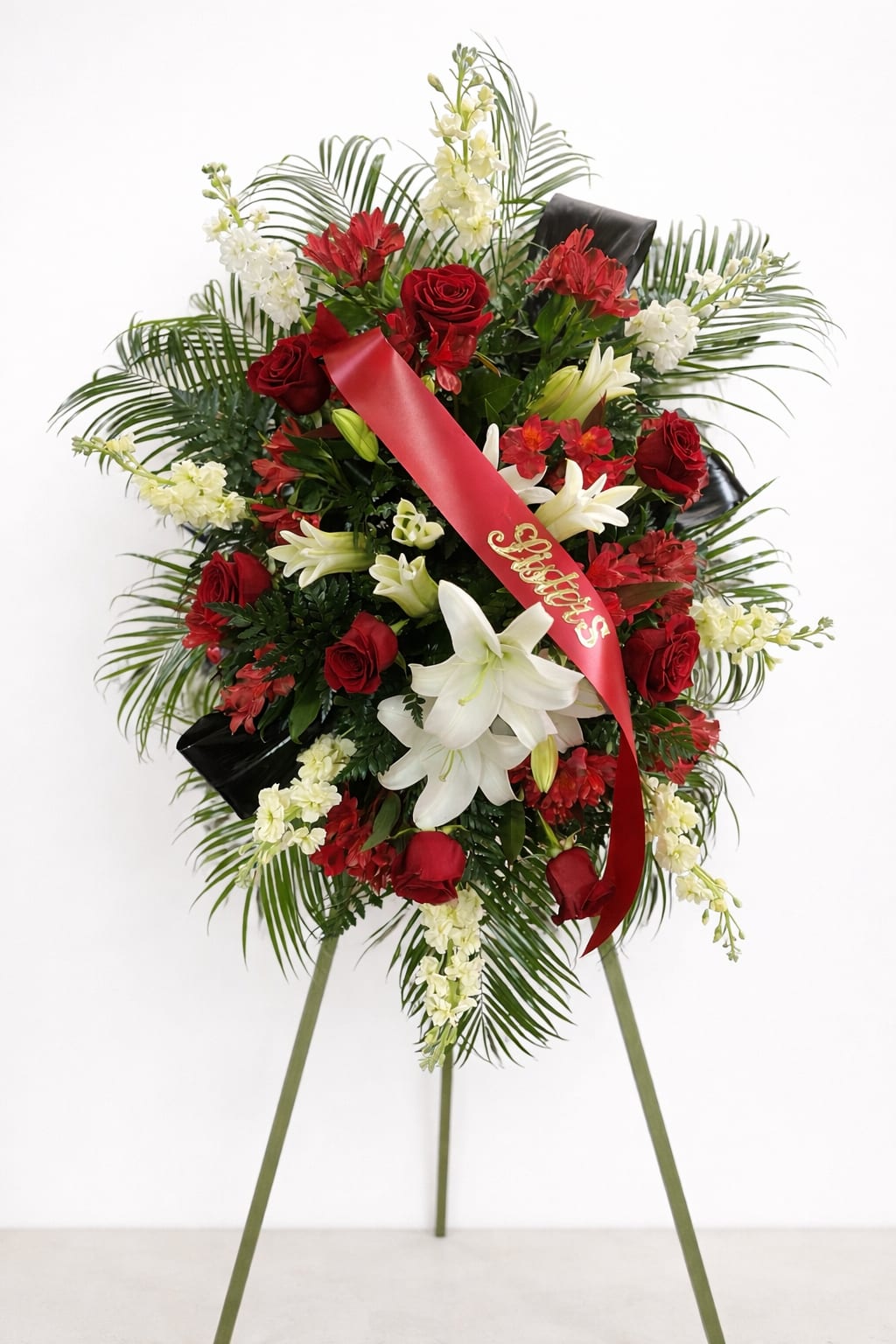 Standing funeral spray of red roses and white lilies with a red ribbon