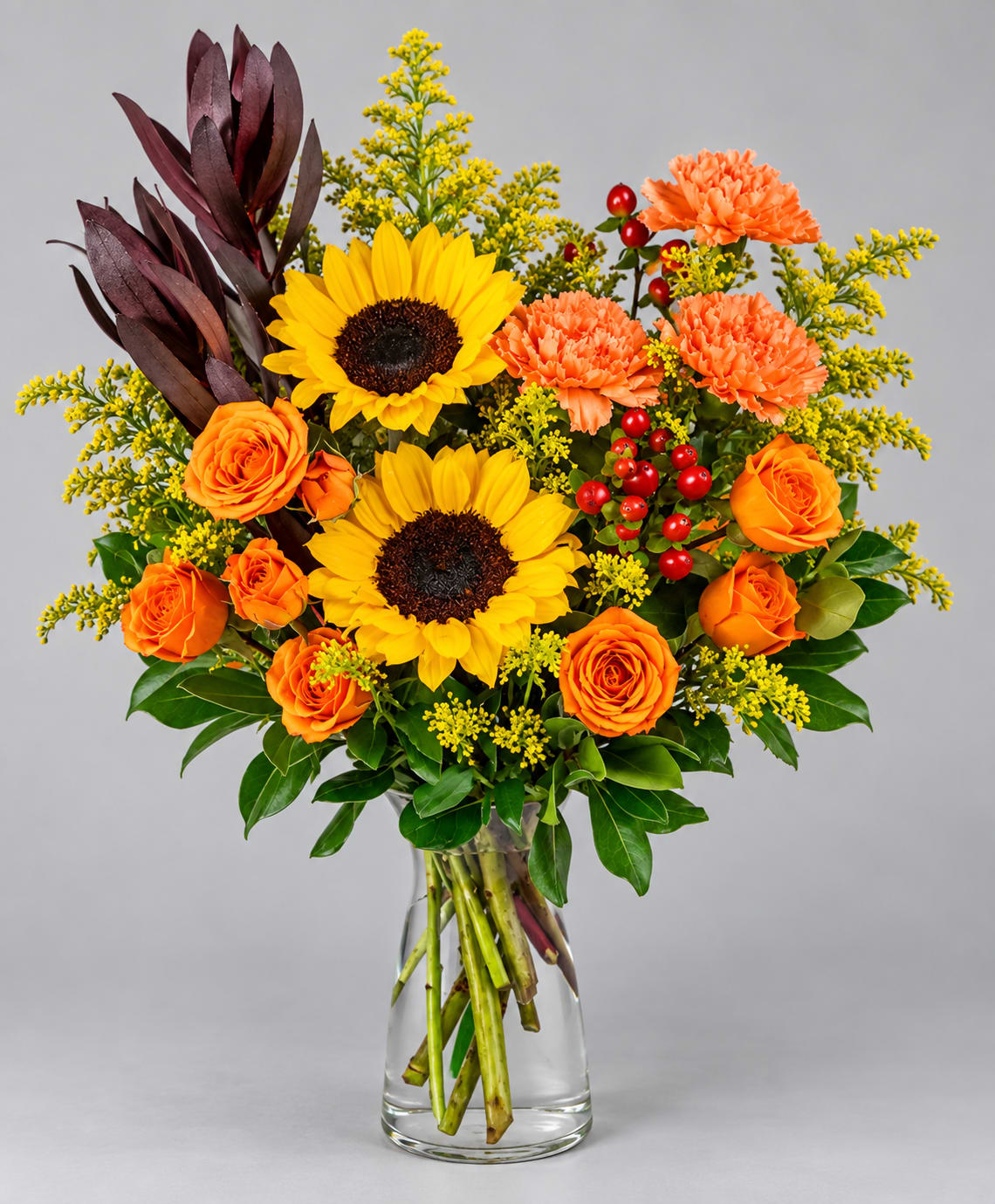 Bouquet of sunflowers, orange roses, and carnations in a clear glass vase