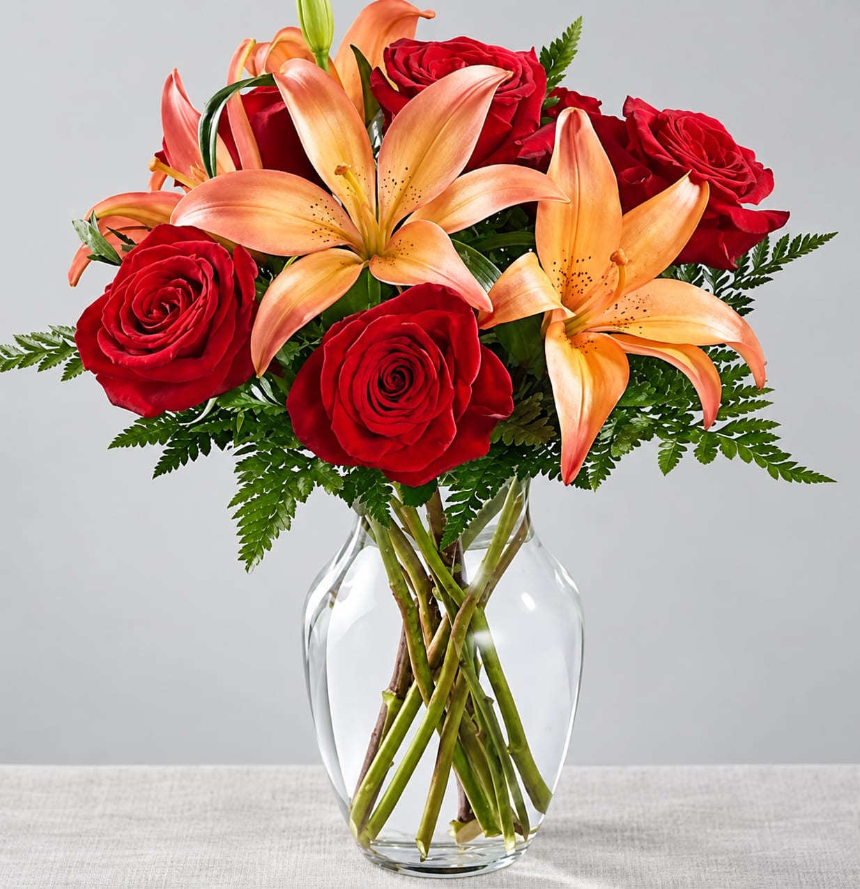 Red roses and peach lilies in a clear glass vase