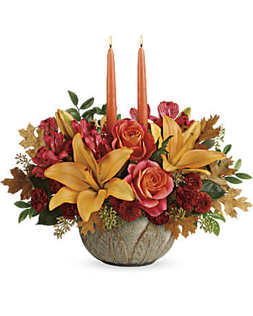 Autumn floral centerpiece with roses, lilies, and two taper candles in a bowl vase