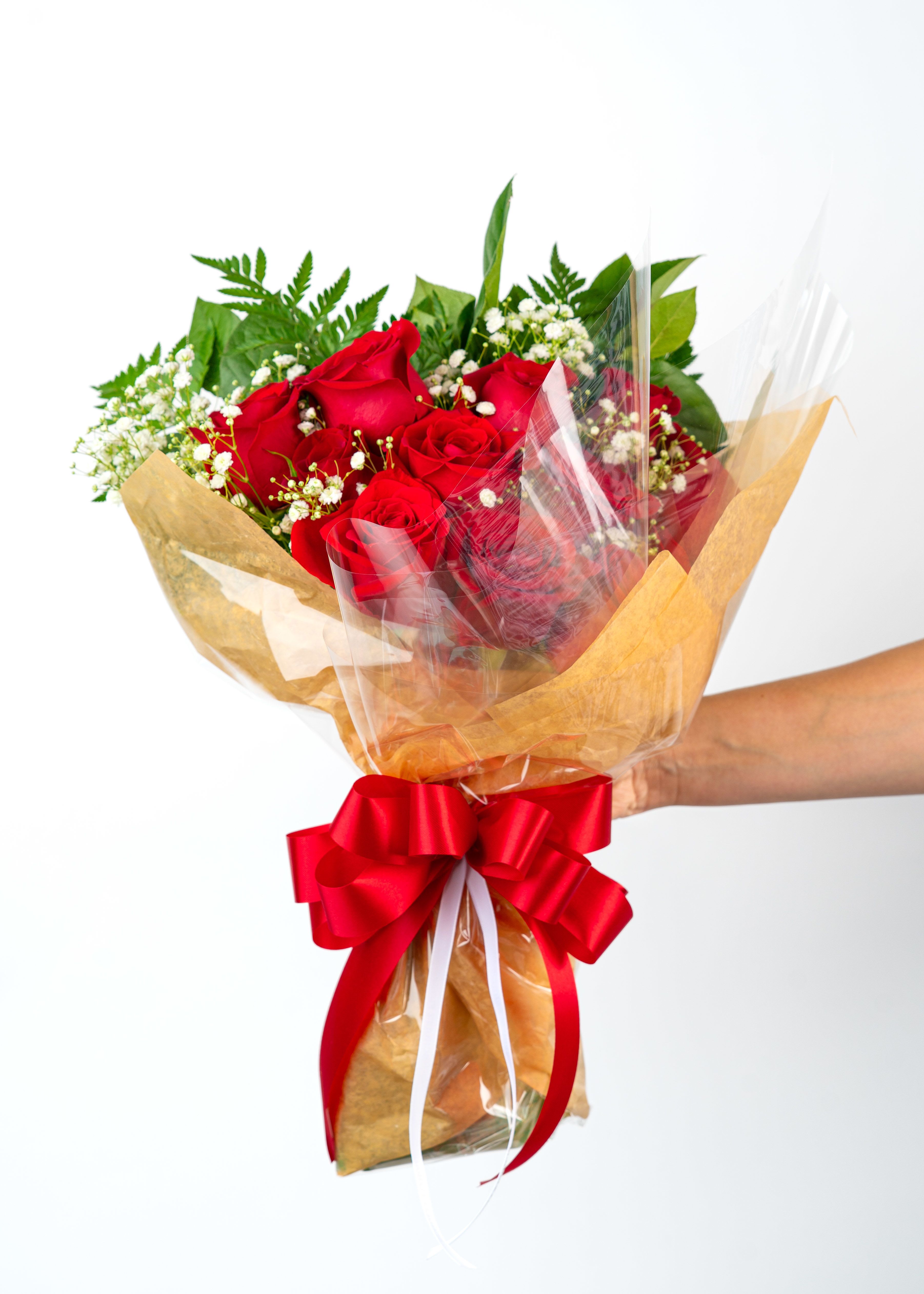 Handheld bouquet of red roses with white filler flowers wrapped in paper and cellophane with a red bow