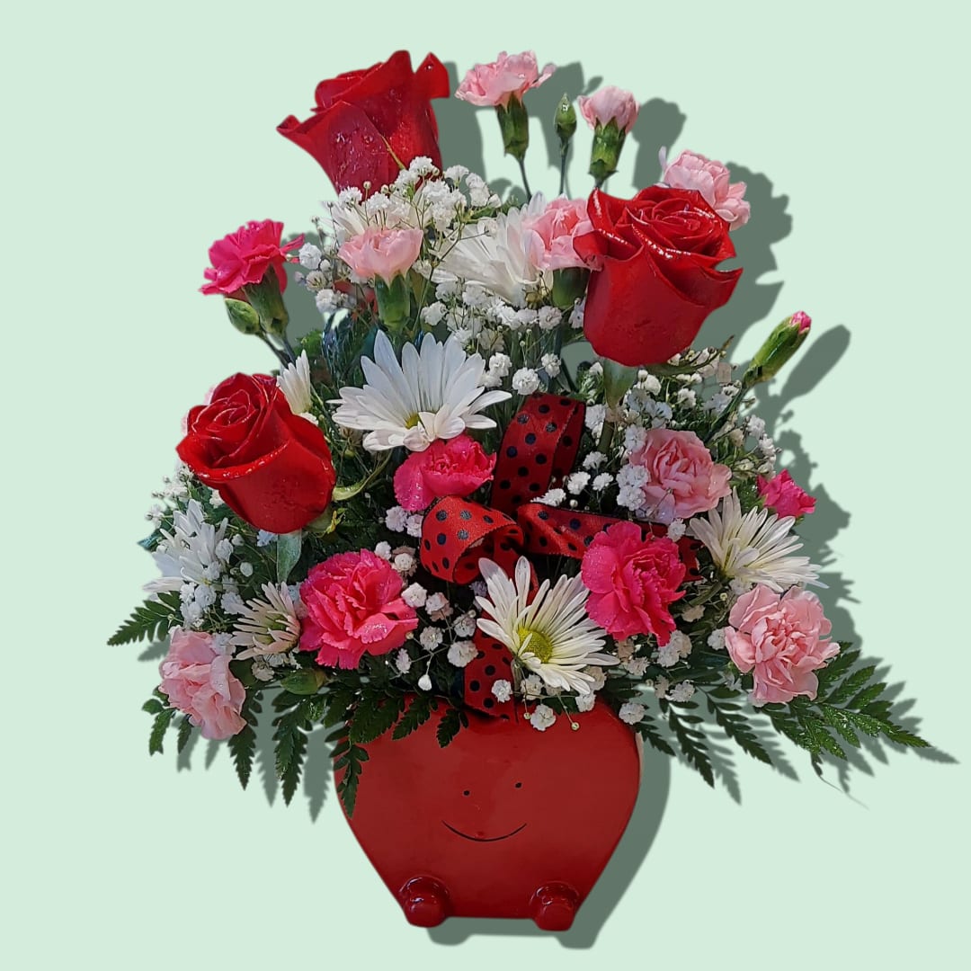 Red and pink flower arrangement in a red smiling pot