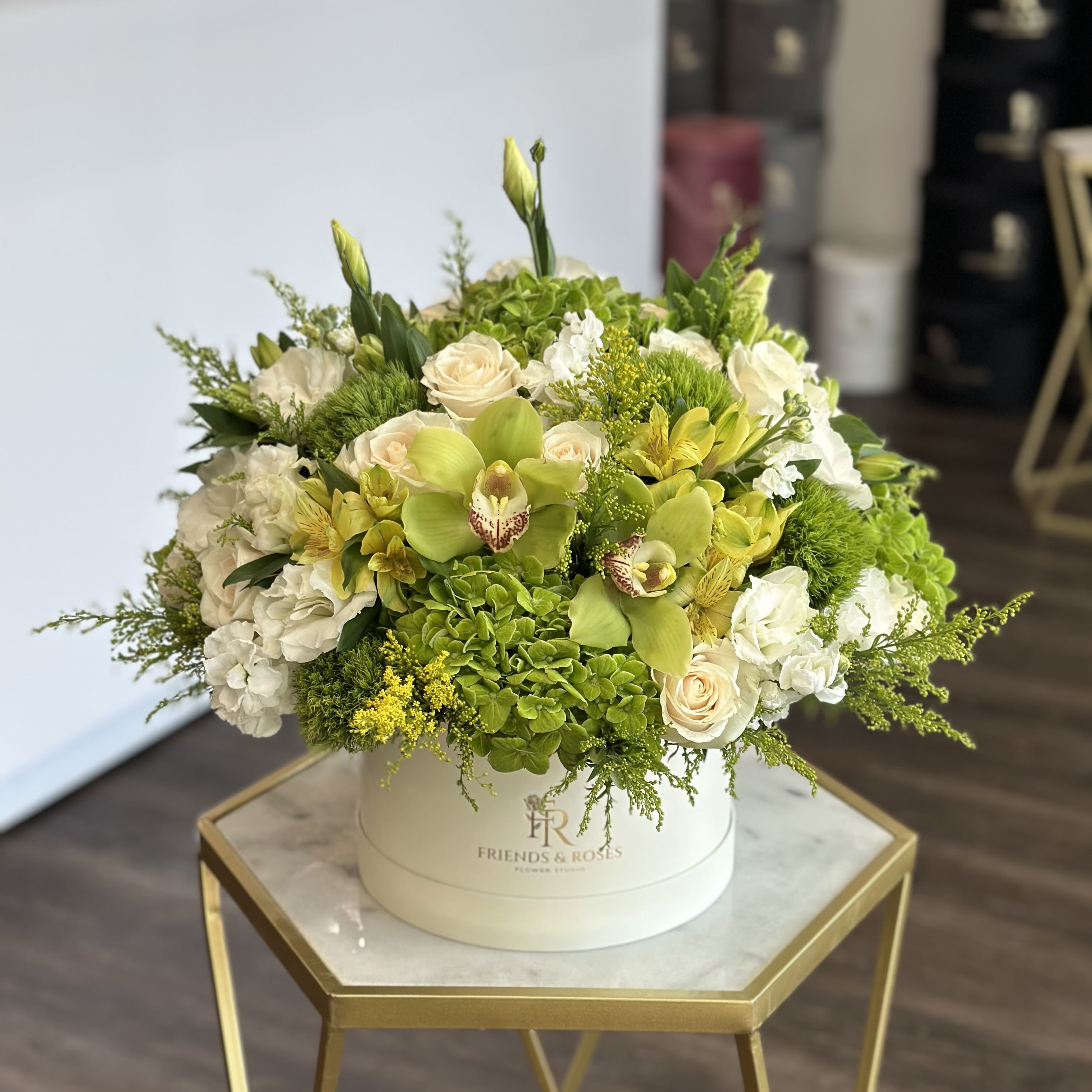 Round floral arrangement in a white hat box with white and green blooms