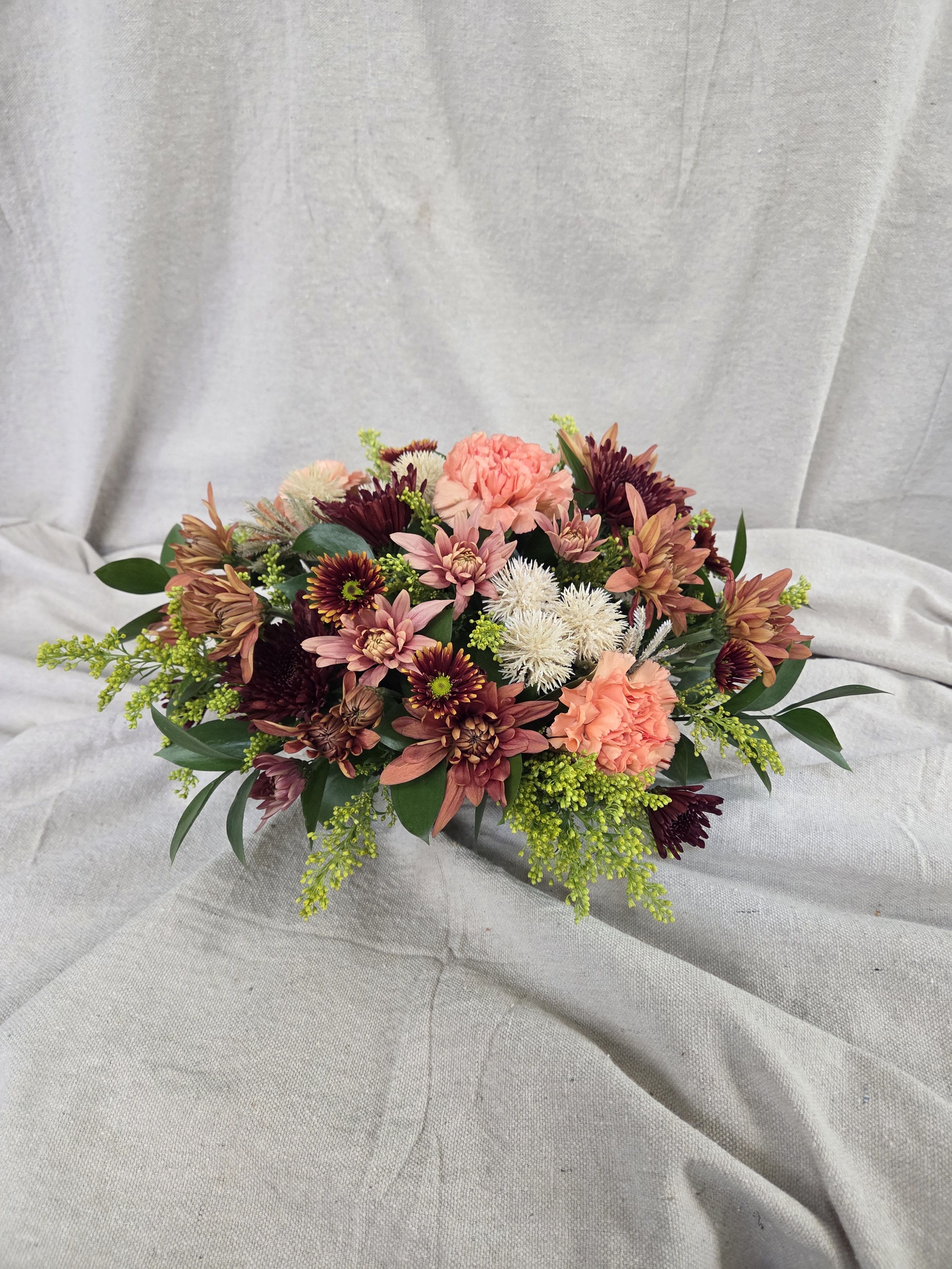 Low arrangement of peach carnations and burgundy chrysanthemums on a neutral draped backdrop