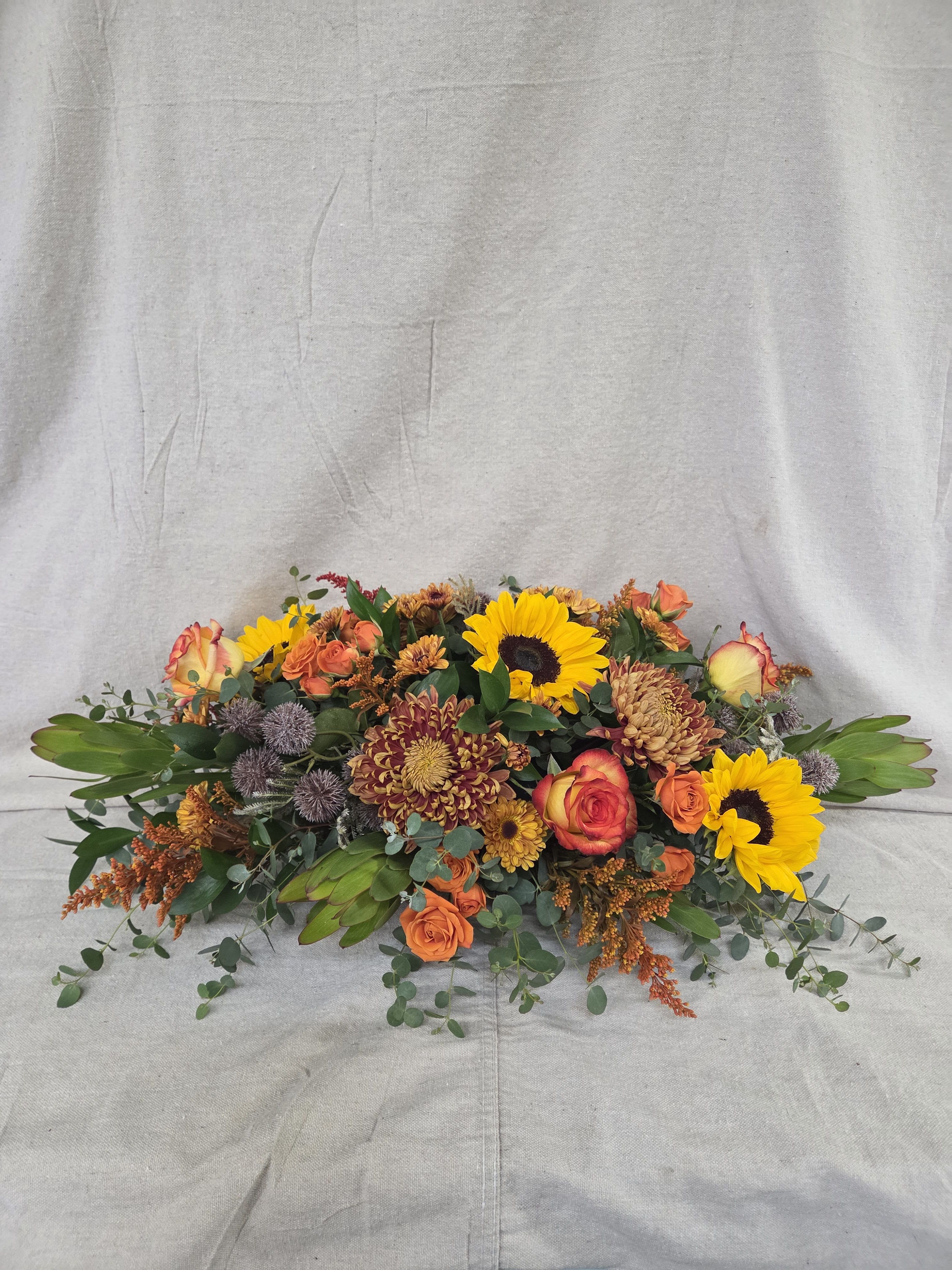 Low autumn centerpiece with sunflowers, orange roses, and bronze mums in a long oval design