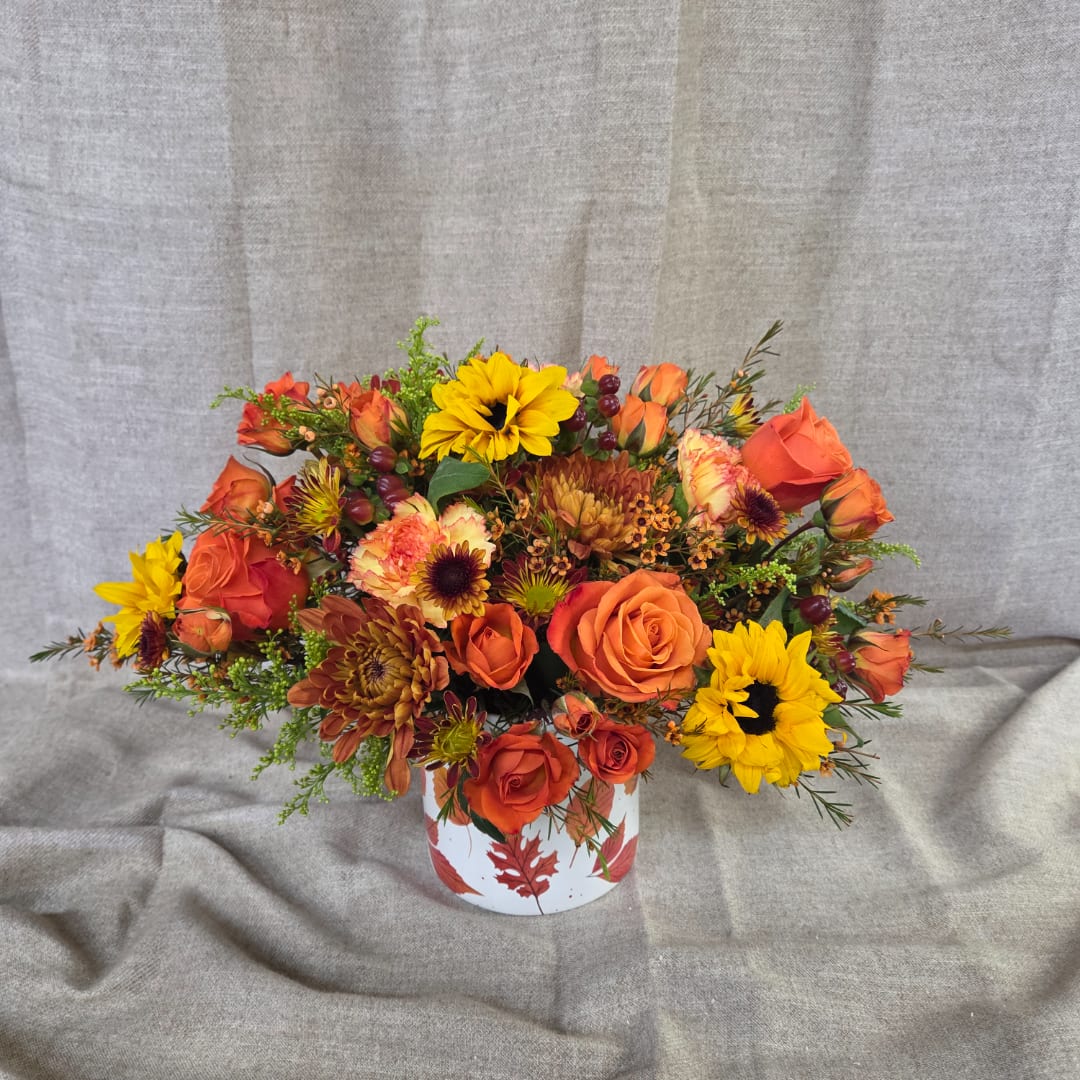 Orange and yellow flower arrangement in a white vase with leaf print
