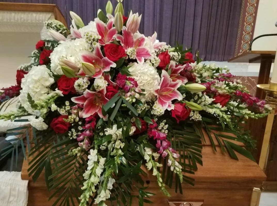 Elegance &amp; Sophistication Casket Spray - This large and graceful casket spray offers a beautiful tribute, filled with a lush combination of premium roses, hydrangea, stargazer lilies, and snapdragons. Designed with care and reverence, the arrangement is accented with tropical foliage to add depth and natural elegance. This timeless floral display conveys love, honor, and heartfelt remembrance during life’s most meaningful moments.  Please note: Floral variety may vary based on seasonal availability, ensuring each arrangement is fresh and unique