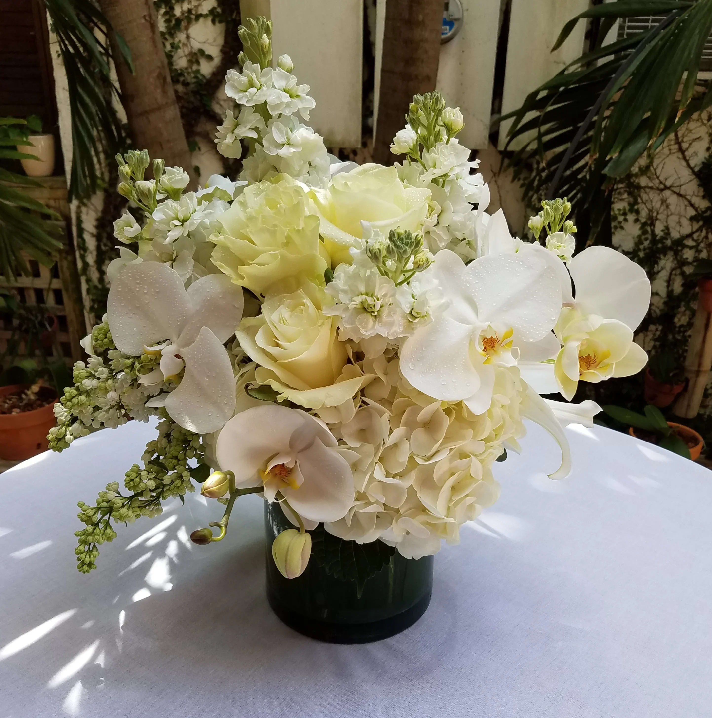 White floral arrangement in a dark vase with orchids and roses