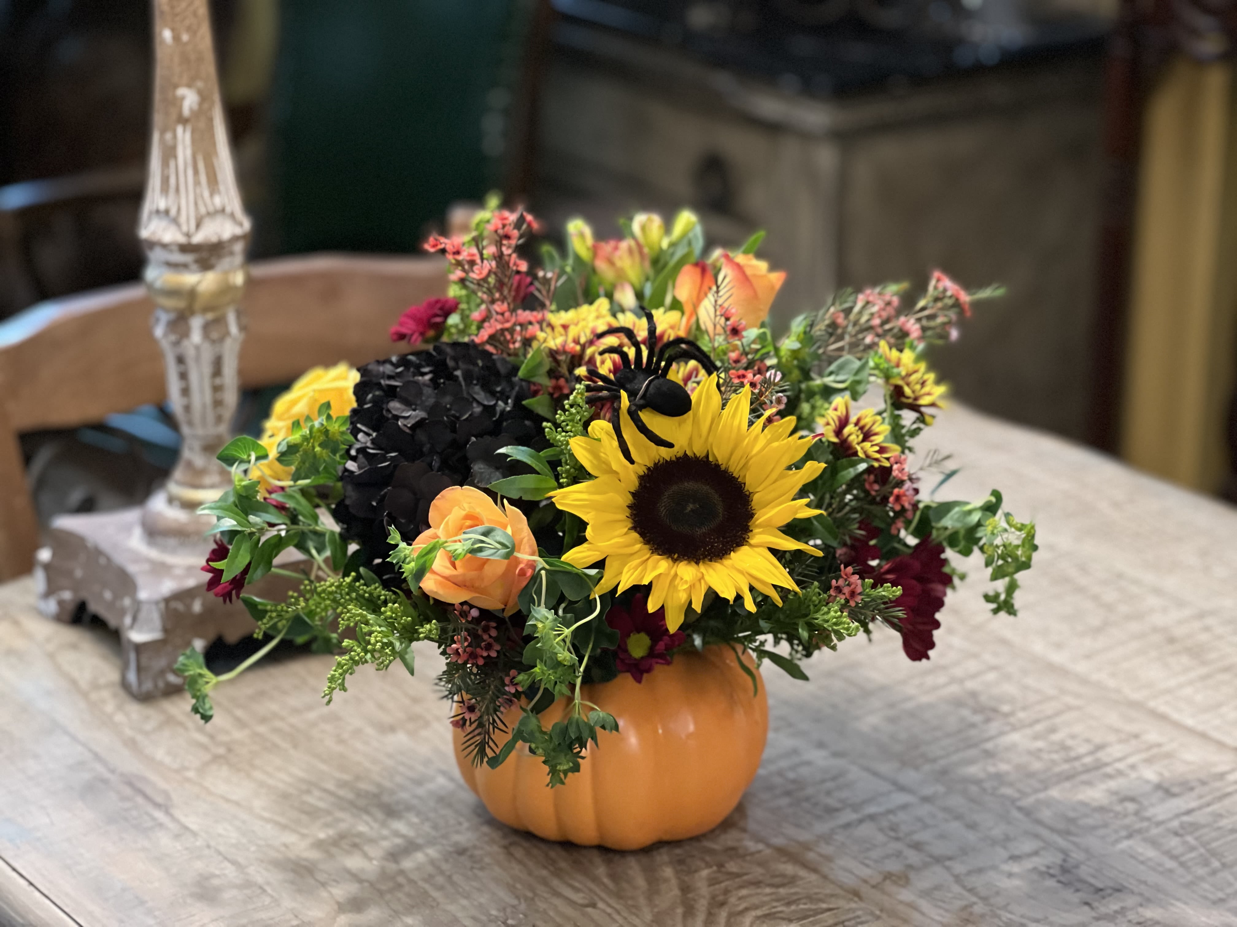 Fall floral arrangement in a pumpkin container with a sunflower and orange roses