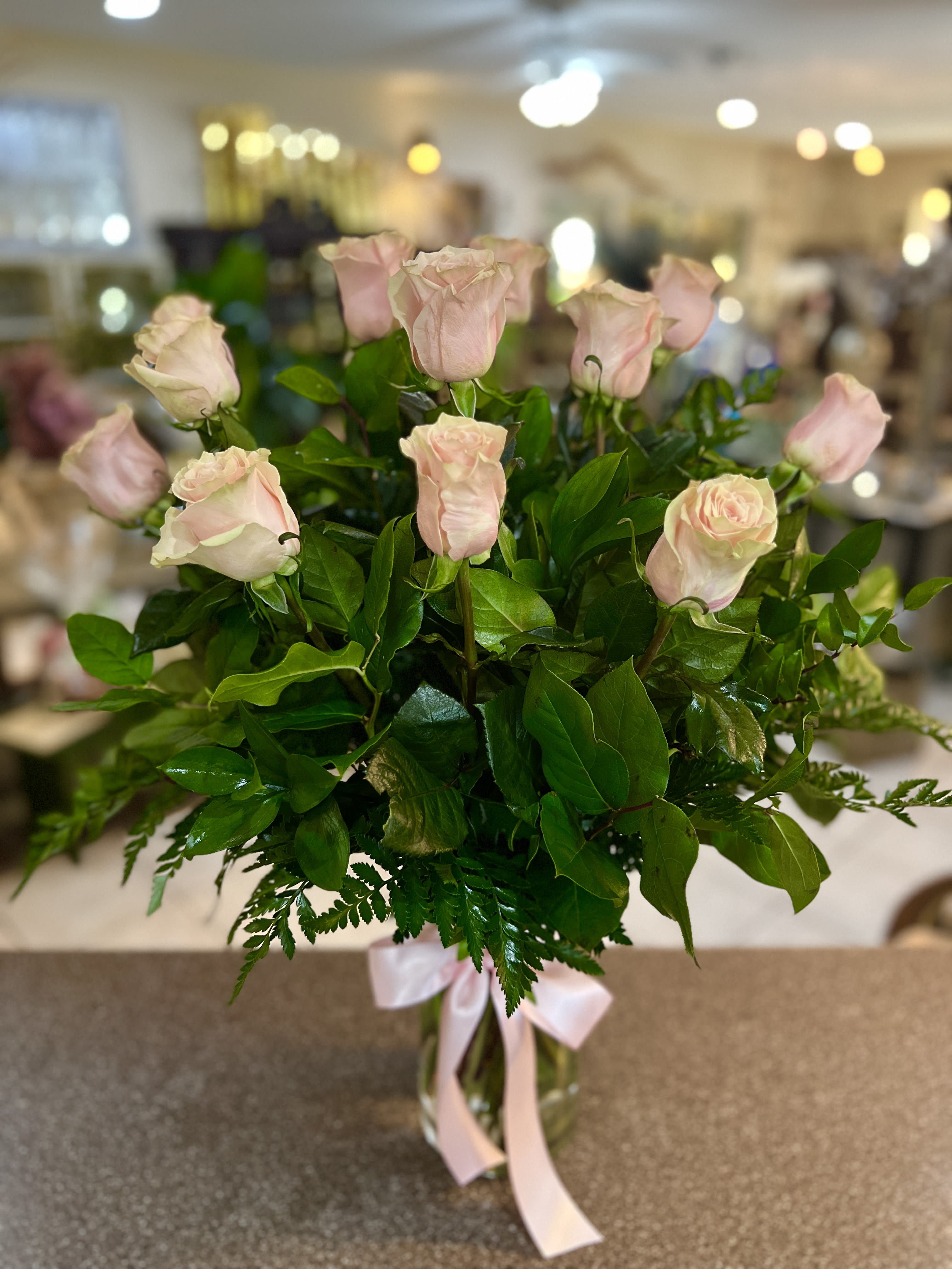 Bouquet of pale pink roses in a clear glass vase with a pink ribbon