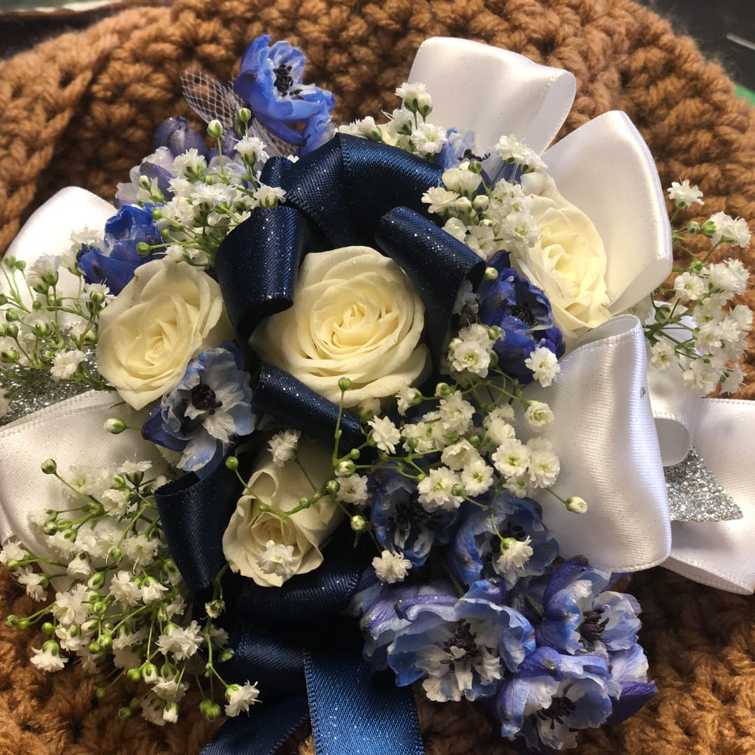 White roses and blue flowers arranged with ribbon on a brown textured background