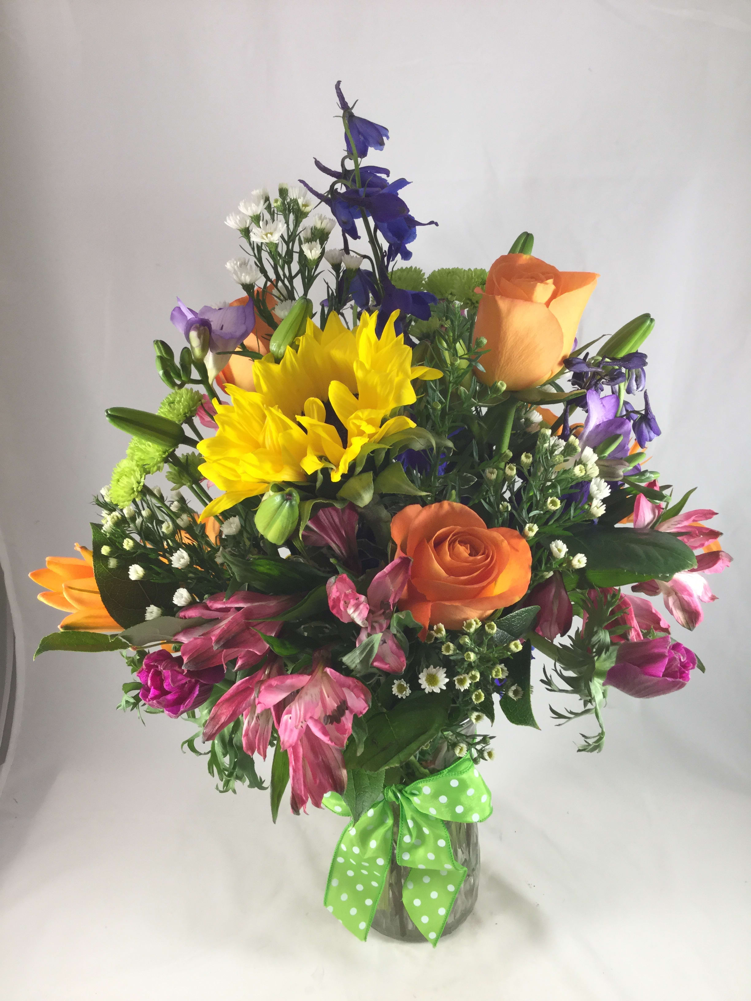 Color Me Happy - A bright festive mix of the season's best flowers, accented with a colorful ribbon