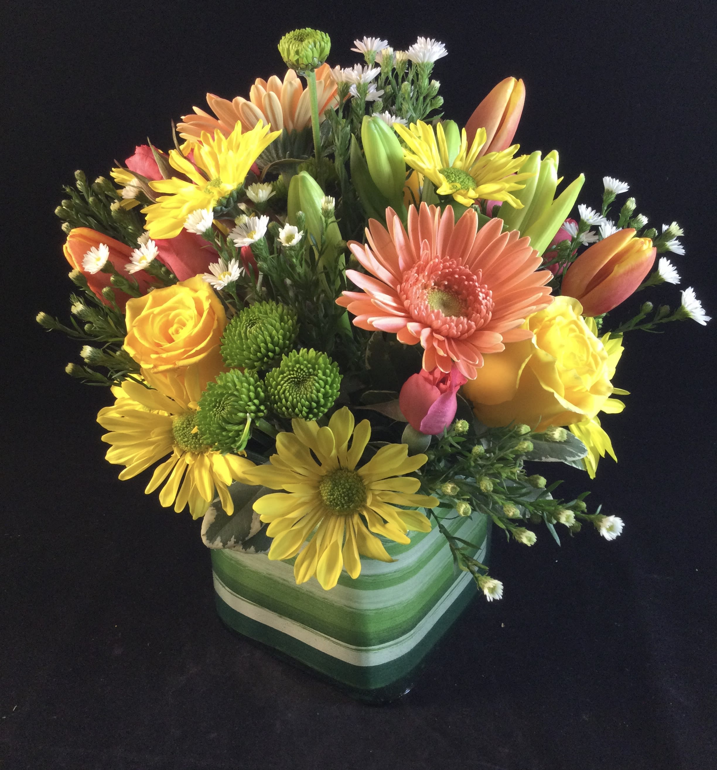 Mixed bouquet of yellow, orange, pink, and white flowers in a green striped vase