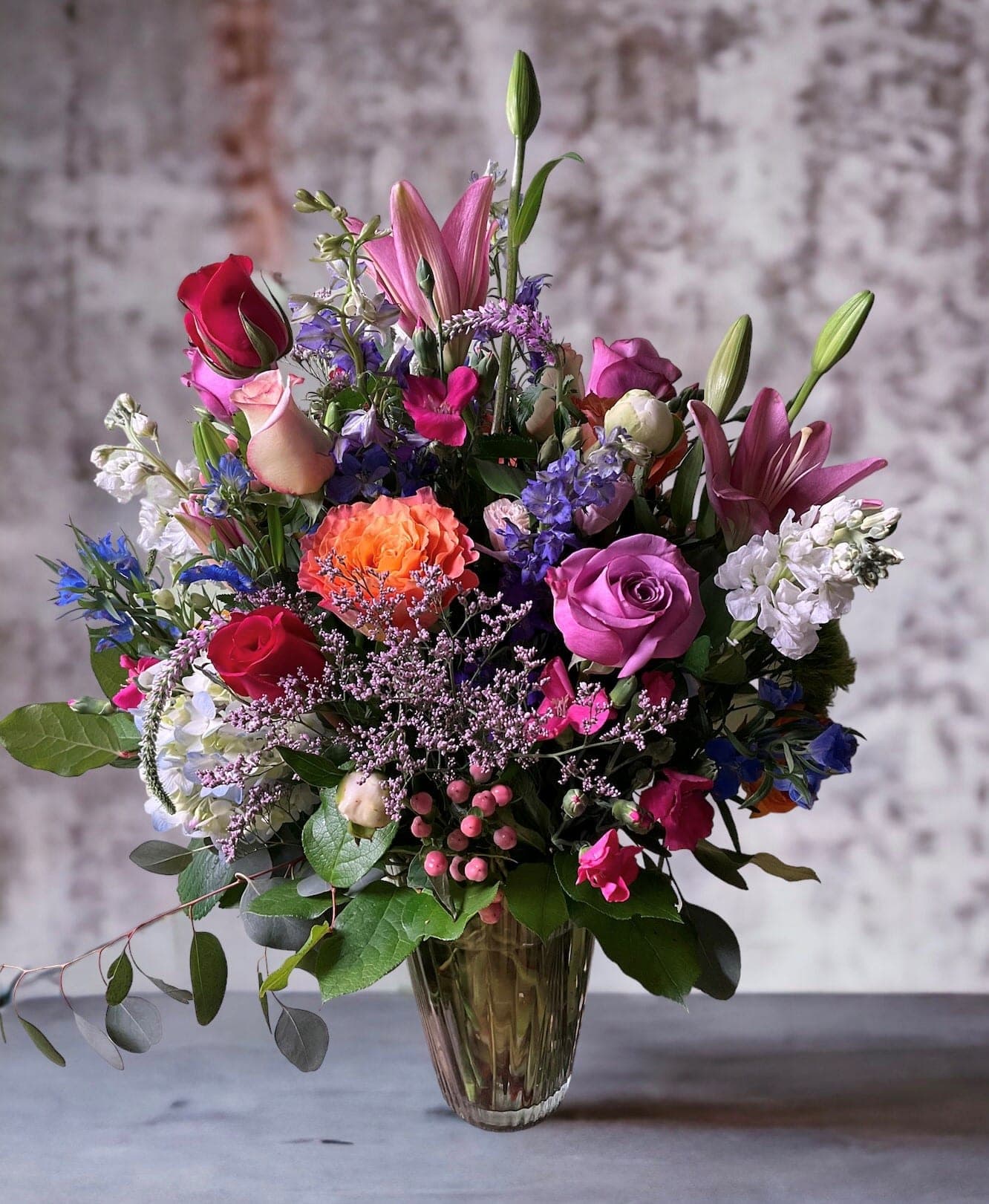 Mixed bouquet of roses, lilies, and purple flowers in a glass vase