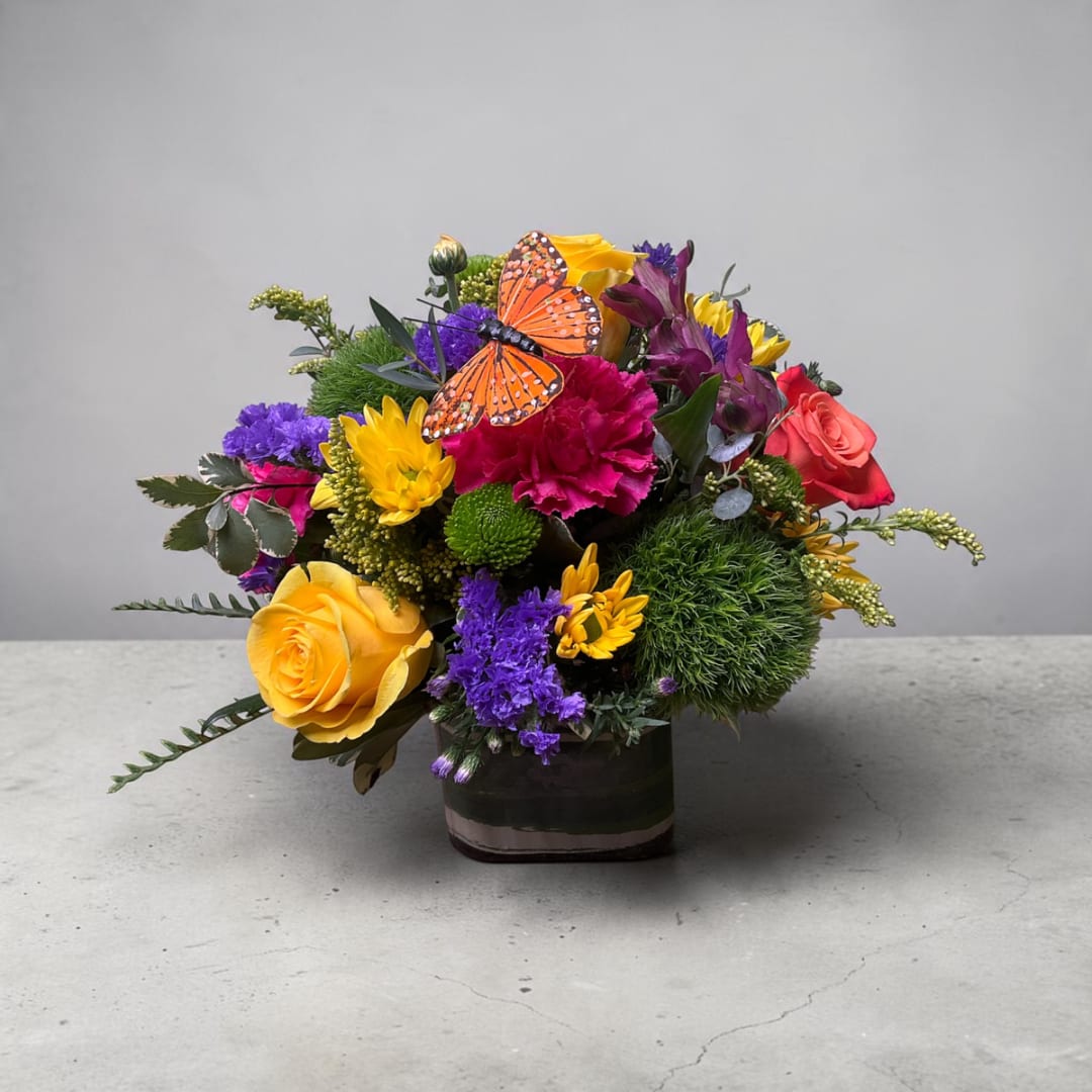 Colorful mixed bouquet in a square vase with a butterfly decoration