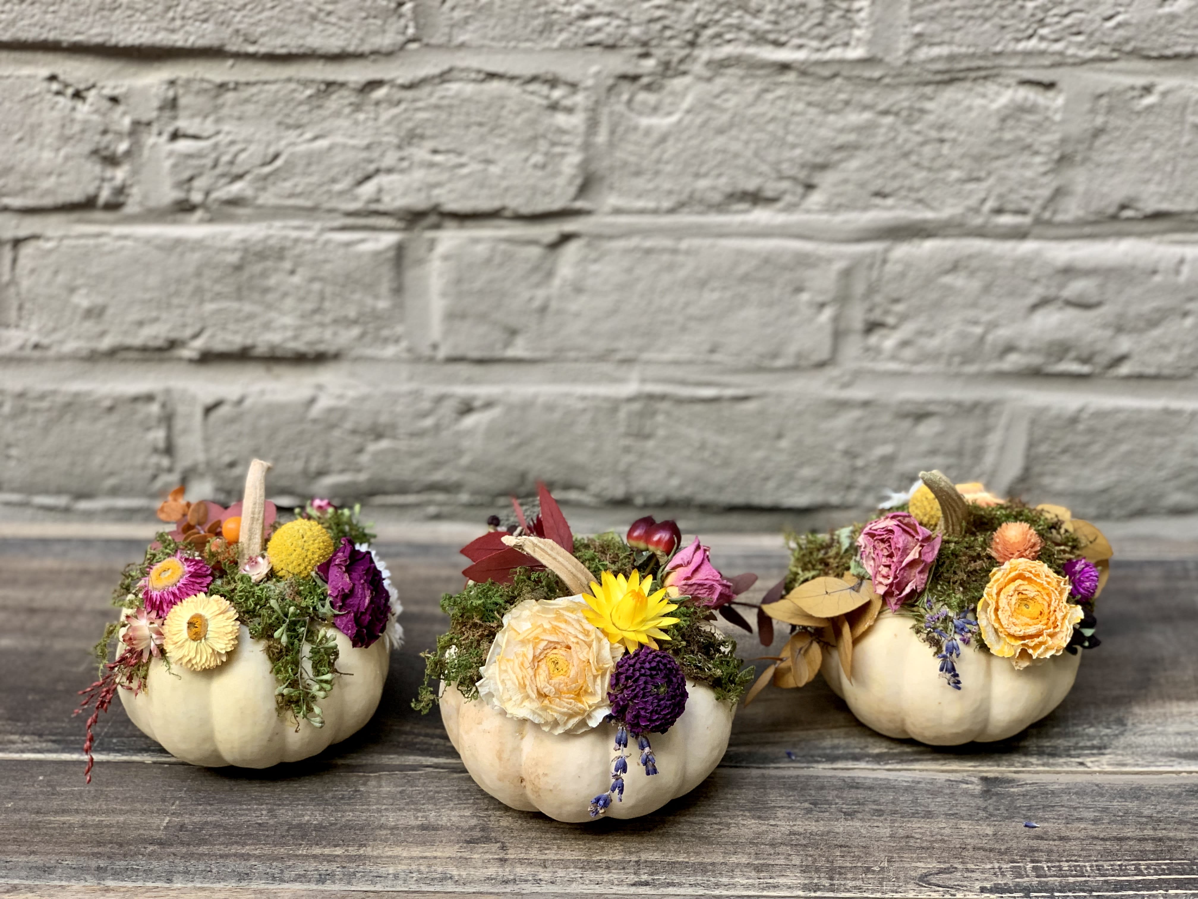 Three small pumpkins decorated with dried flowers and moss