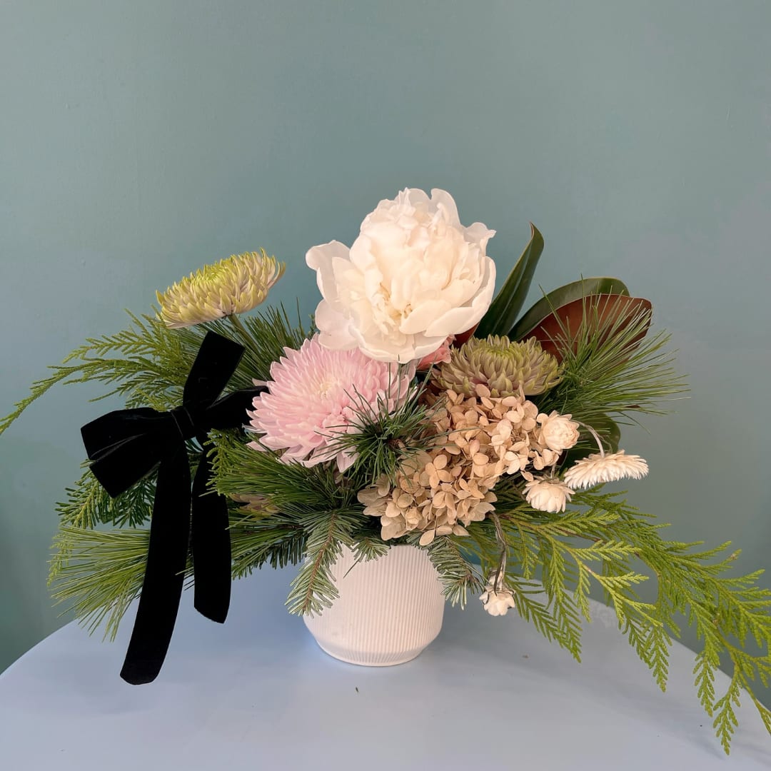 Floral arrangement in a white vase with pink and cream blooms and a black ribbon