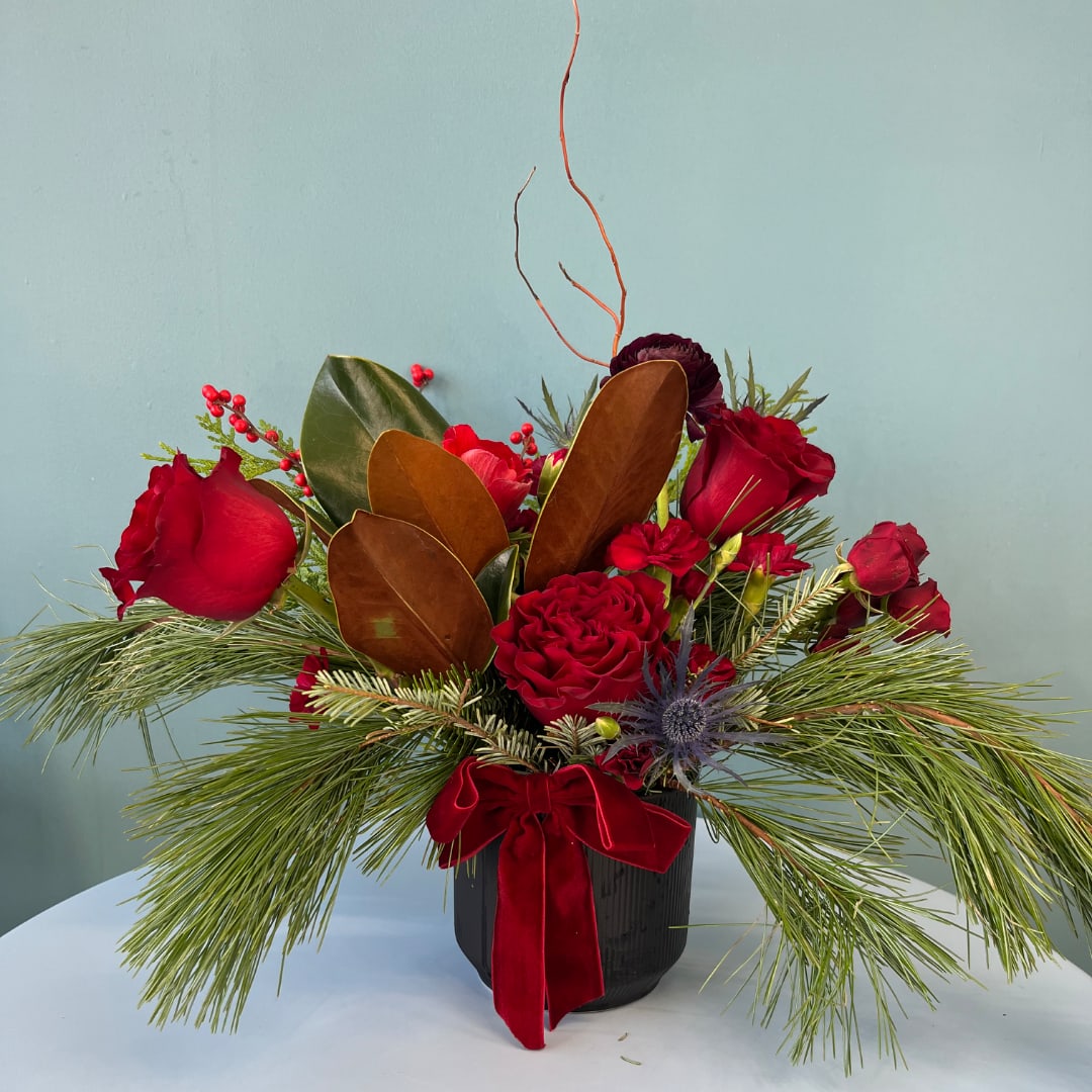 Red roses arranged in a black vase with pine and a red ribbon