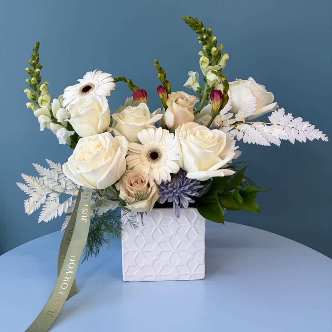 White roses and gerbera daisies arranged in a square ceramic vase