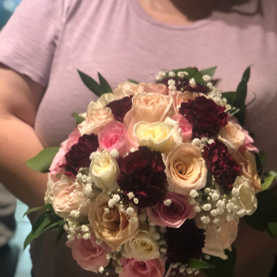 Handheld bouquet of pink, cream, and burgundy roses with baby's breath