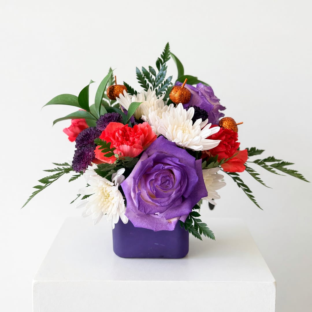Purple and red floral arrangement in a square vase with small pumpkin picks