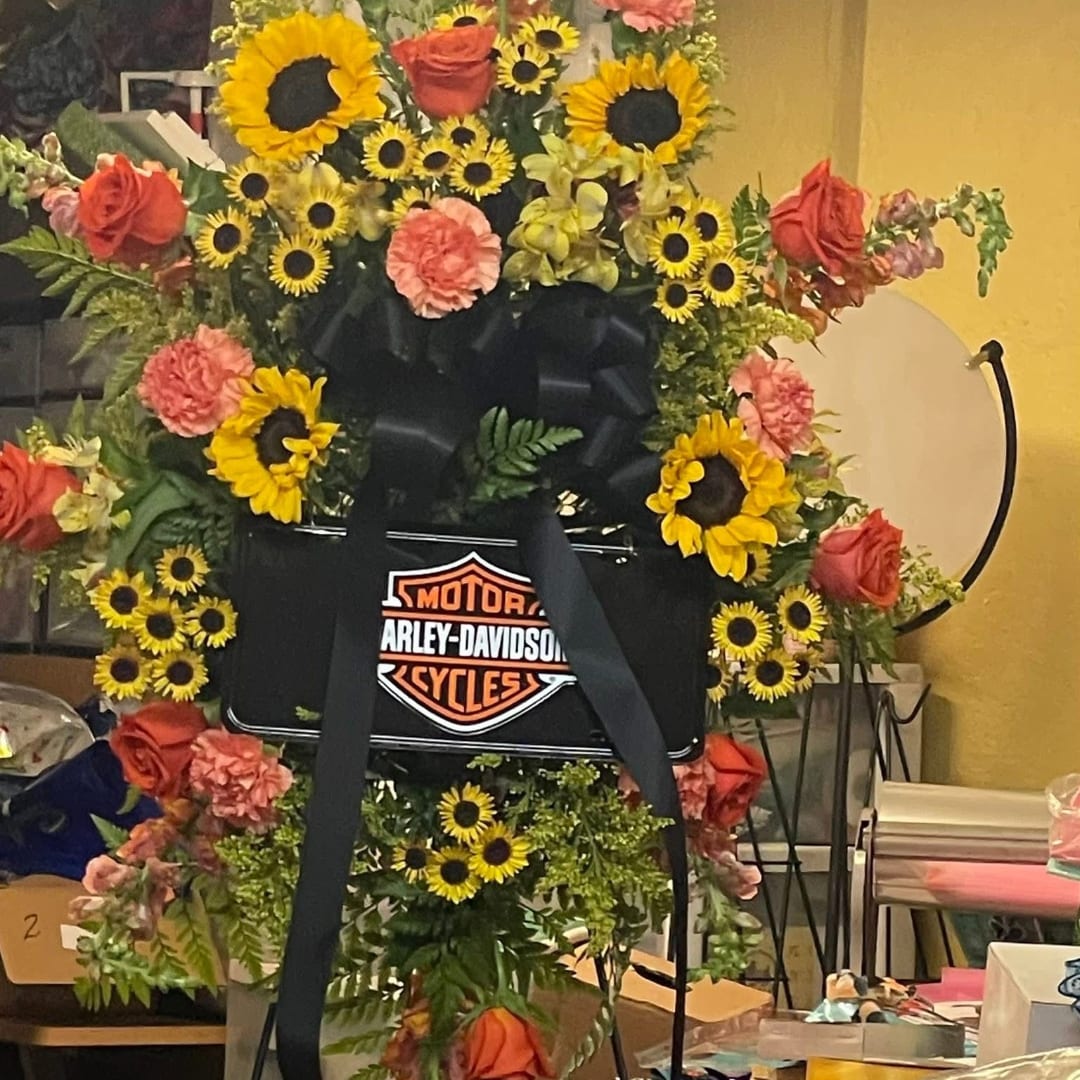 Large floral wreath with sunflowers, roses, and carnations around a Harley-Davidson sign