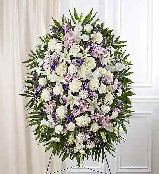 Lavender And White Funeral Standing Spray - When words alone cannot convey the feelings in your heart, flowers can provide a meaningful and profound statement. Our impressive standing spray arrangement is meticulously handcrafted by expert local florists with soothing lavender and white blooms for a lush, full presentation, presenting an elegant and memorable tribute.Standing spray arrangement with lavender daisy poms, stock and monte casino; white roses, Oriental lilies, football mums, gladiola and carnations; purple statice; accented with soft, lush greenery