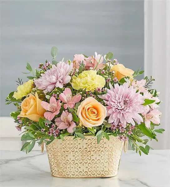 Loving Remembrance  Multicolor Pastel - Celebrate the life of a loved one with our beautiful floral tribute. A mix of blooms in soothing pastel shades is a symbol of enduring love. Designed in our Remembrance Cachepot, featuring an embossed pattern and finished with a gold brushed ivory surface.