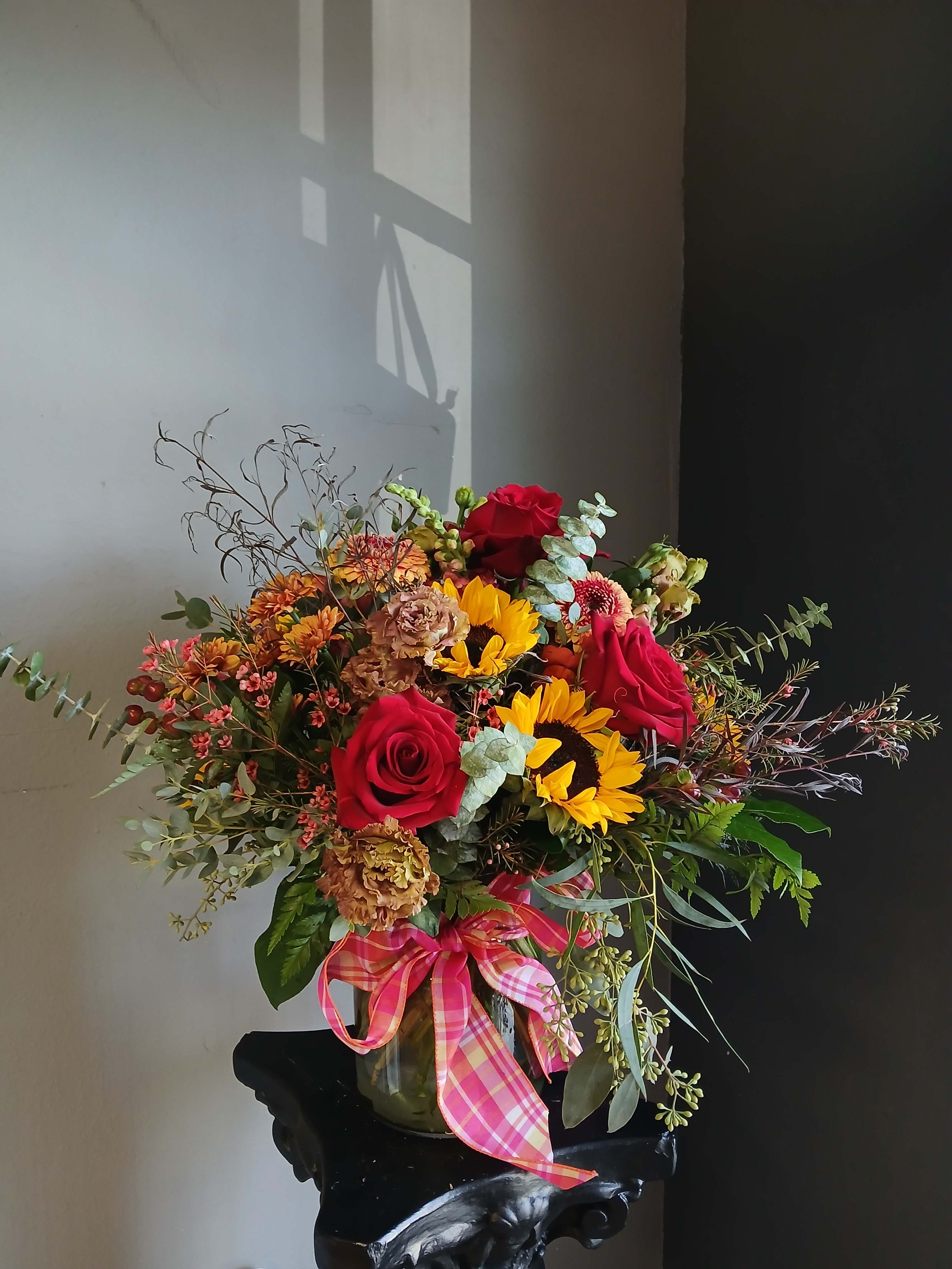 Bouquet of red roses and sunflowers in a glass vase with a pink ribbon