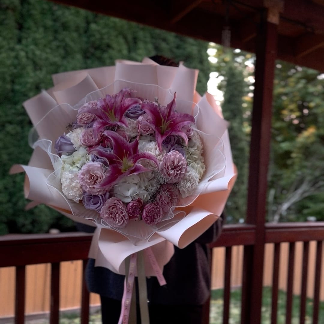 Pink and purple bouquet with lilies and roses wrapped in pale paper
