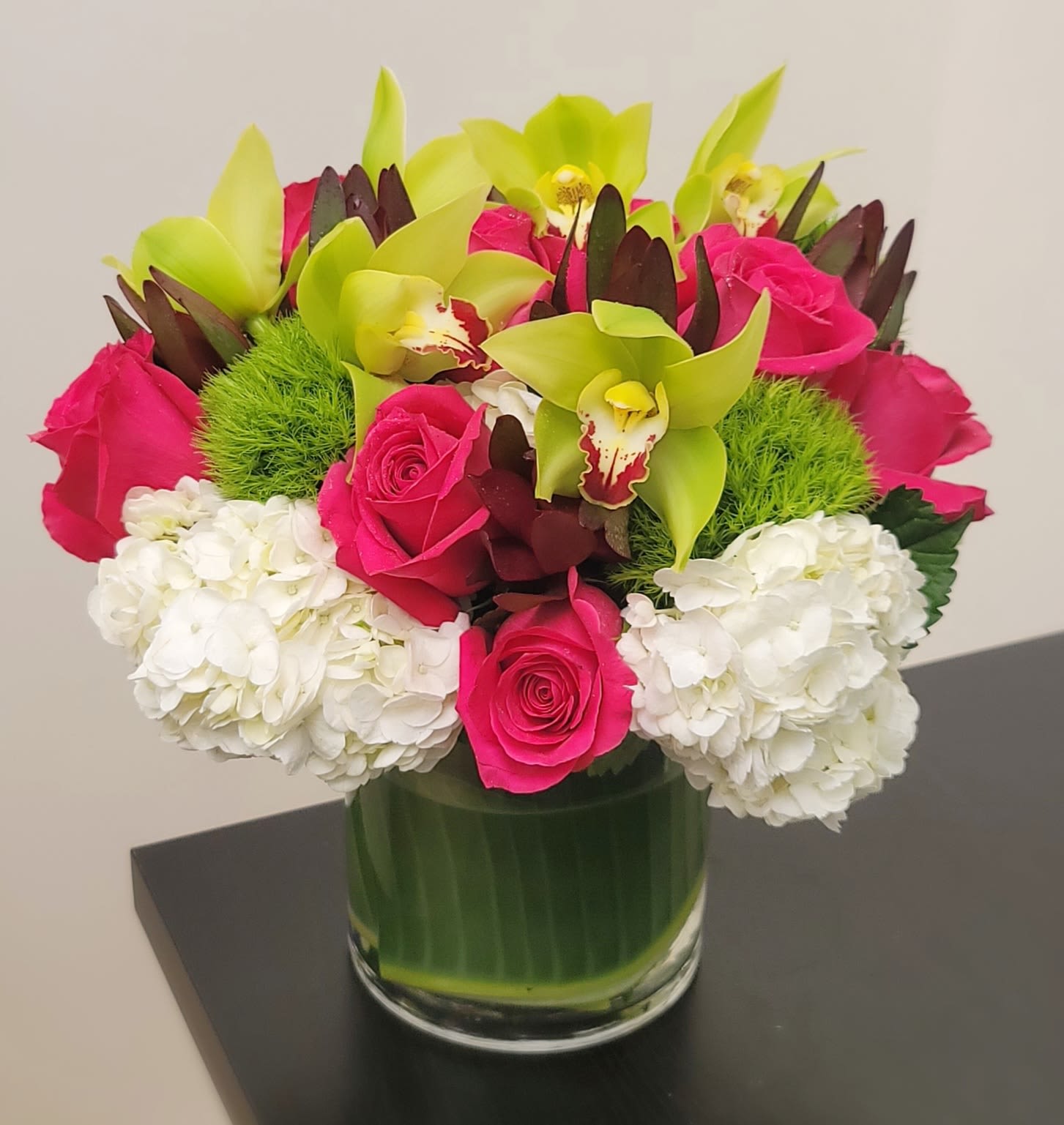 Pink roses and green orchids in a glass vase with white hydrangeas