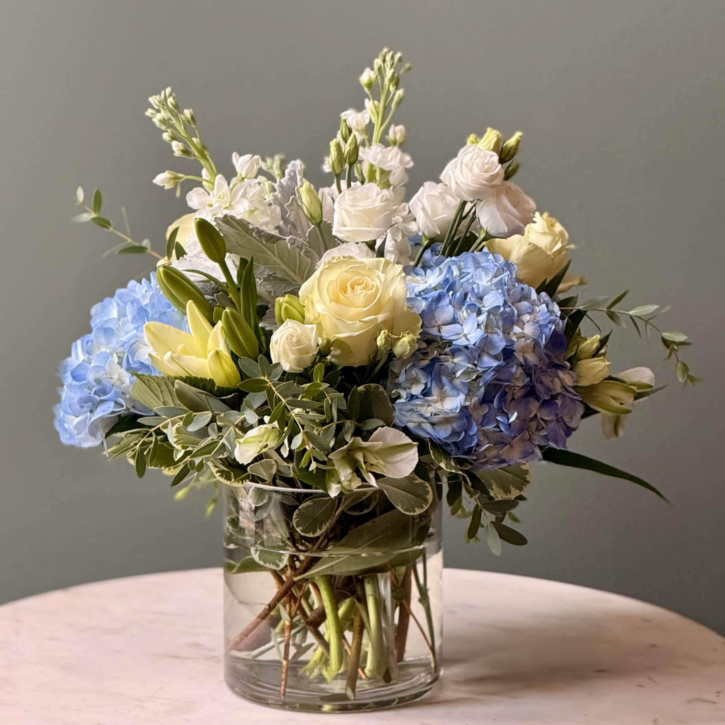 Blue hydrangeas and pale roses arranged in a clear glass vase
