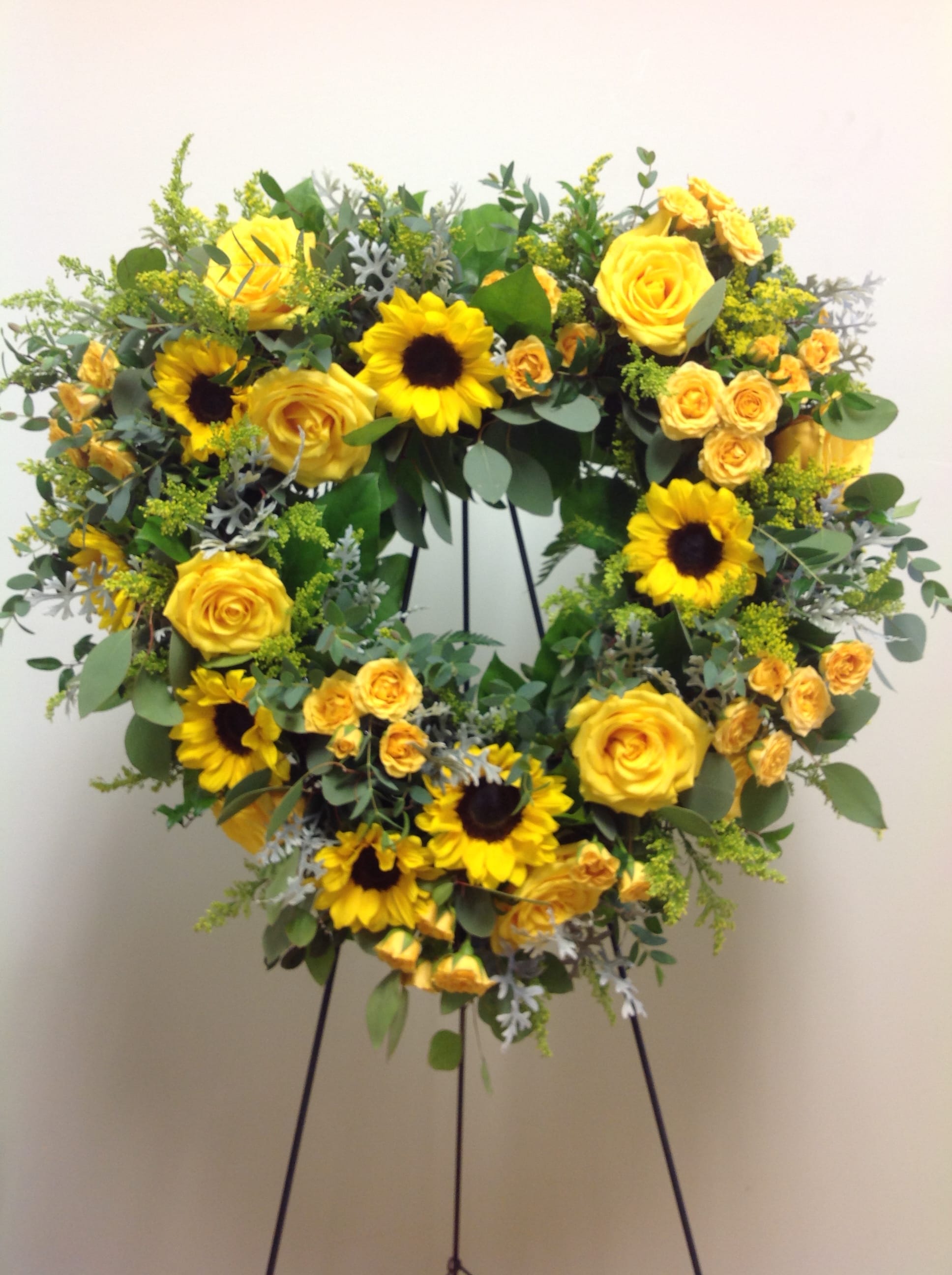 Yellow roses and sunflowers arranged in a wreath on a stand