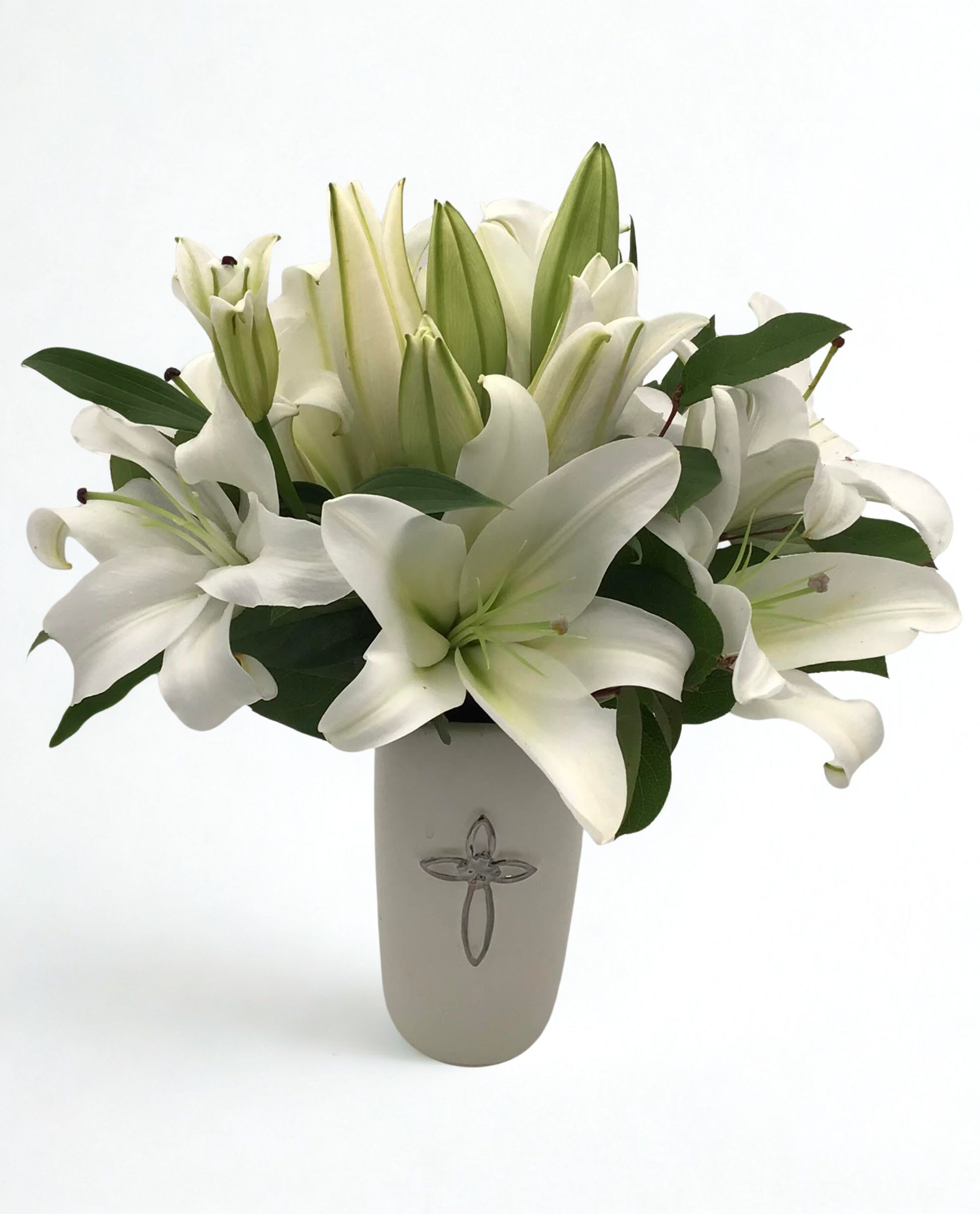 White lilies arranged in a tall vase with dark green leaves