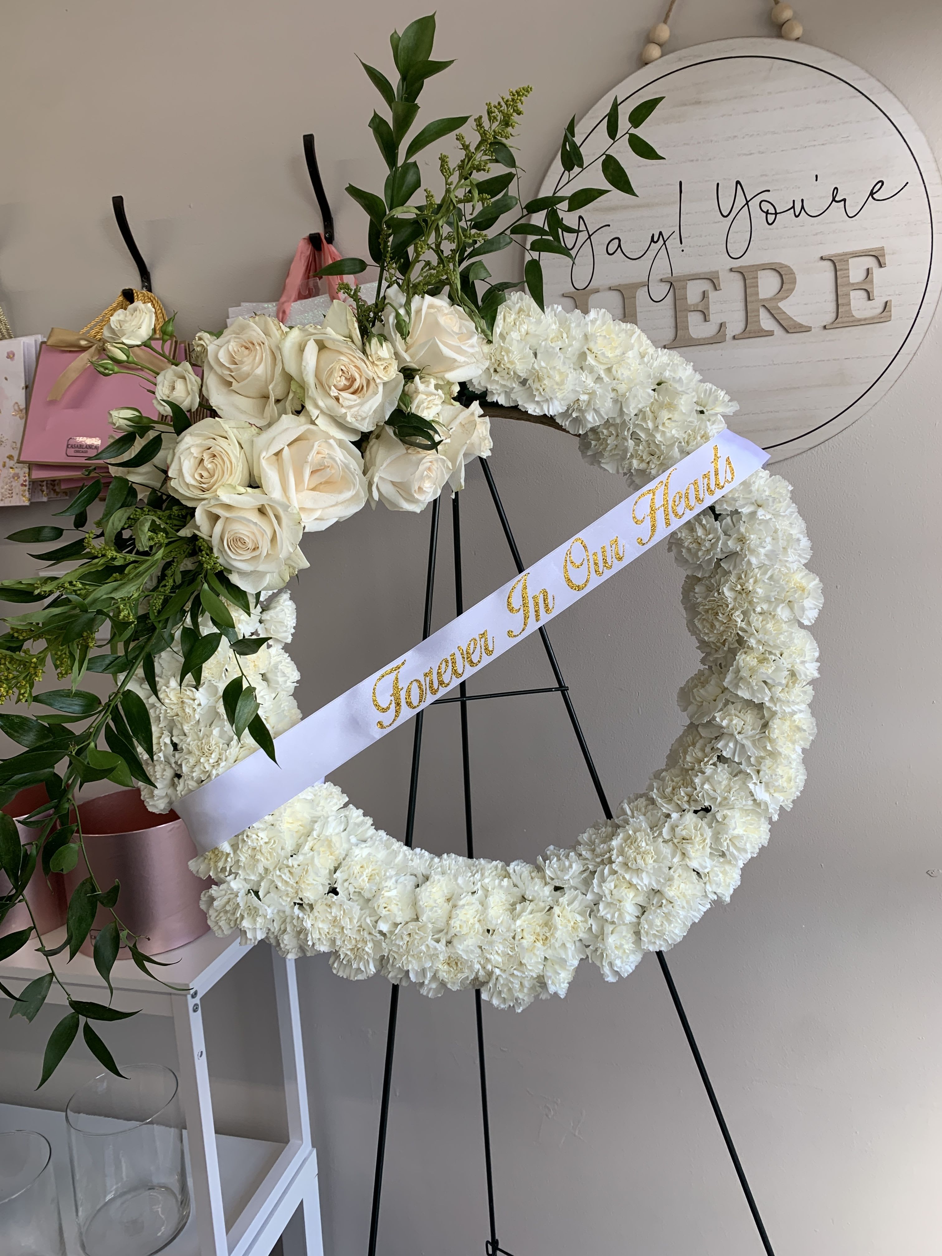 White rose and carnation heart wreath on an easel with a ribbon