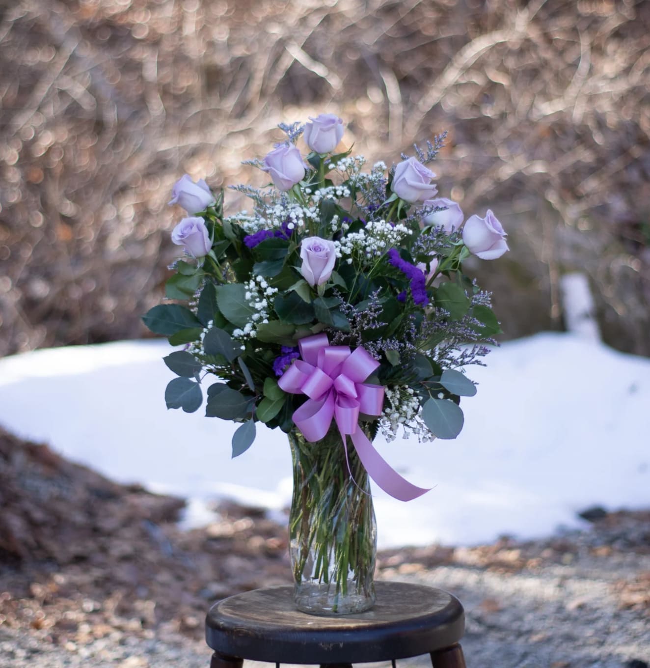 Twilight Dozen Roses (Purple/Lavender) - Beautiful and fragrant lavender roses arranged  in a glass vase. Extra long stem / AAA grade quality. Limited quantity available. Standard will include 12 roses, accent flowers and foliage with a bow, deluxe size will include seasonal accents or branch material, for example, fall- could include dry wheat, winter - pine cones or winter branches, spring - pussy willow or curly willow, summer - curly willow and local garden accent flower. Deluxe size during a holiday - inclusion of holiday decor Valentine's Day decor etc. Premium includes 18 roses and deluxe upgrade elements. We typically get lavender in our assorted weekly rose pack. May require 24-48hour outside high volume times like Valentine's ay week.