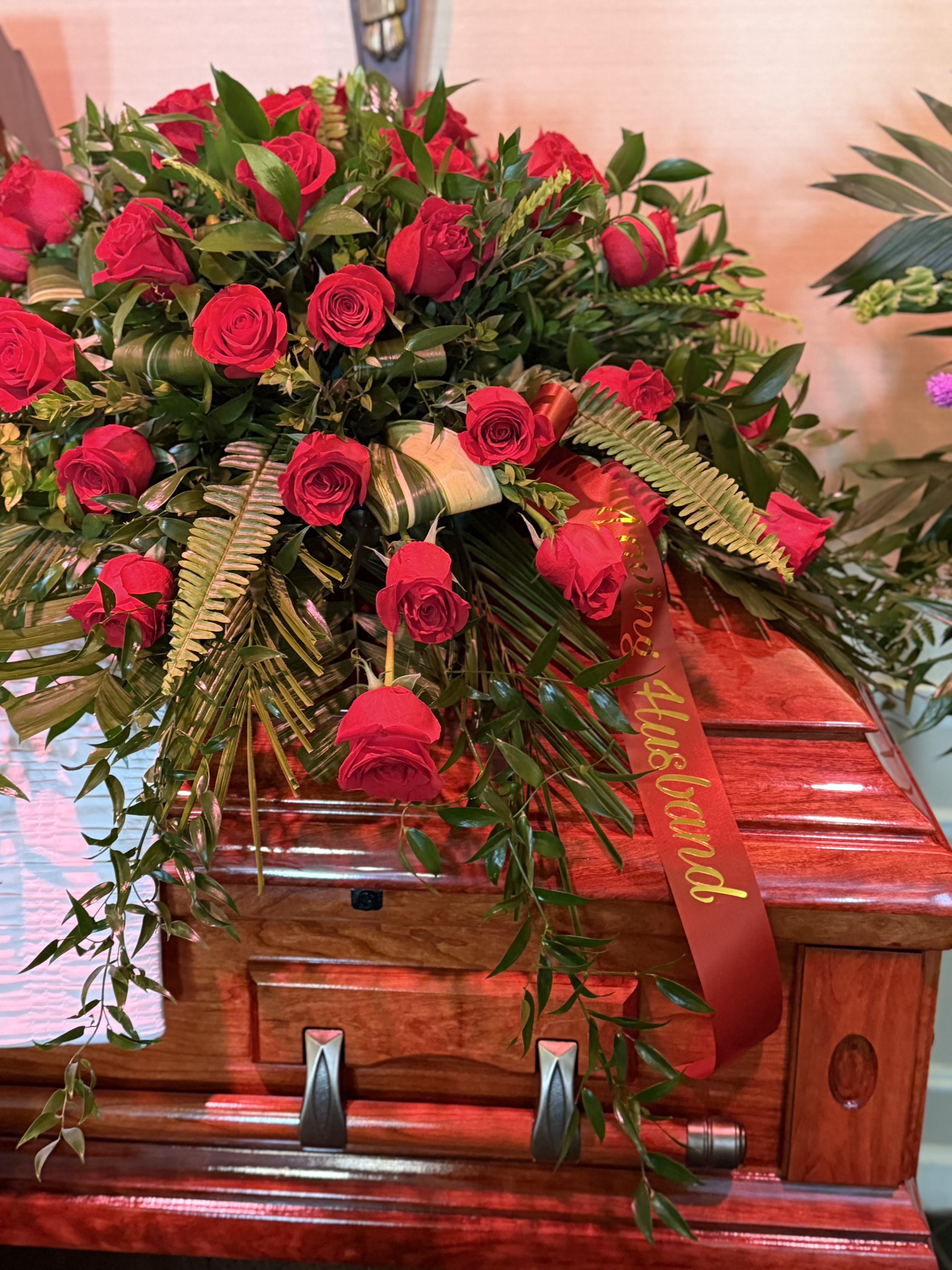 Red rose arrangement on a wooden casket with a red ribbon